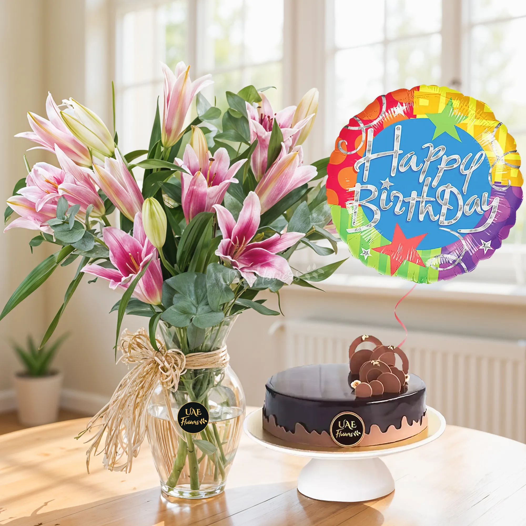 5 pink lilies with green fillers in a clear glass vase with 1 Kg chocolate cake and HAPPY BIRTHDAY Foil Balloon.