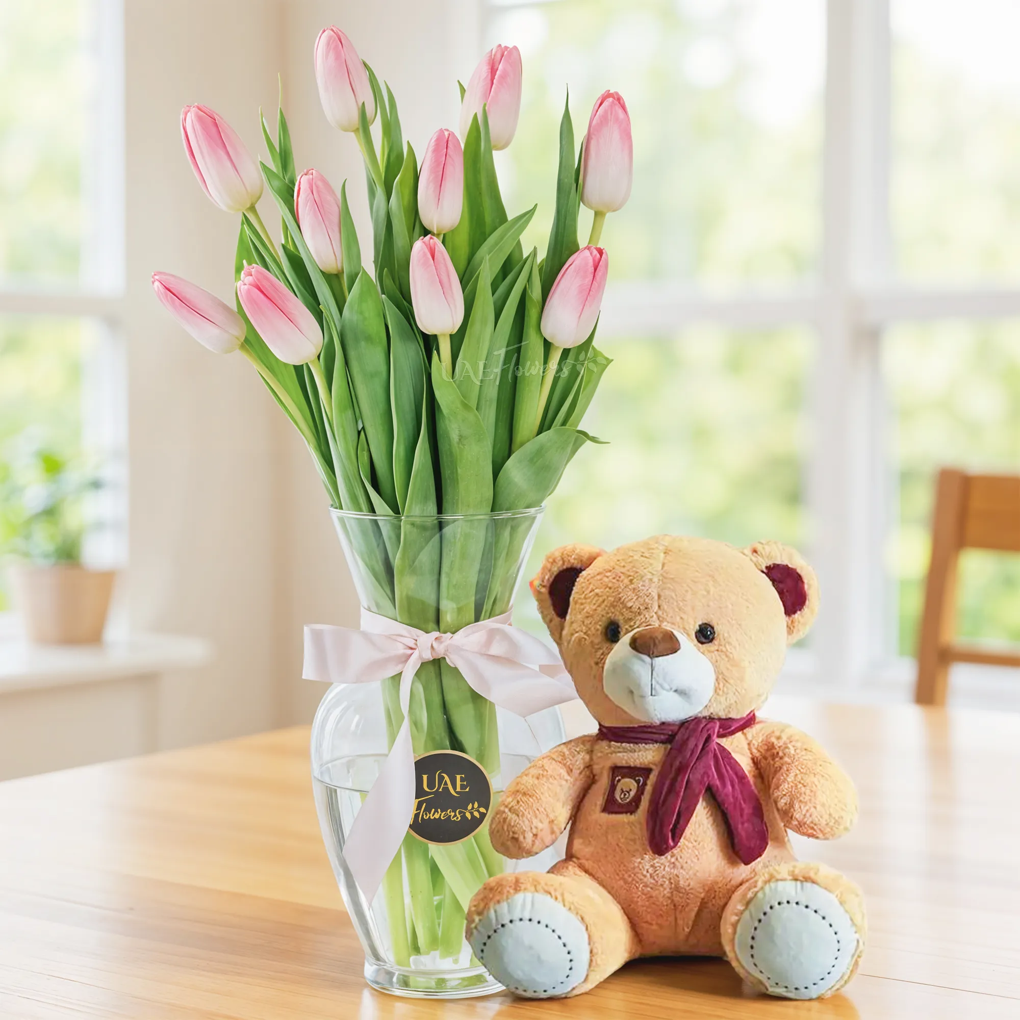 10 pink tulips in a glass vase and a small brown teddy bear.