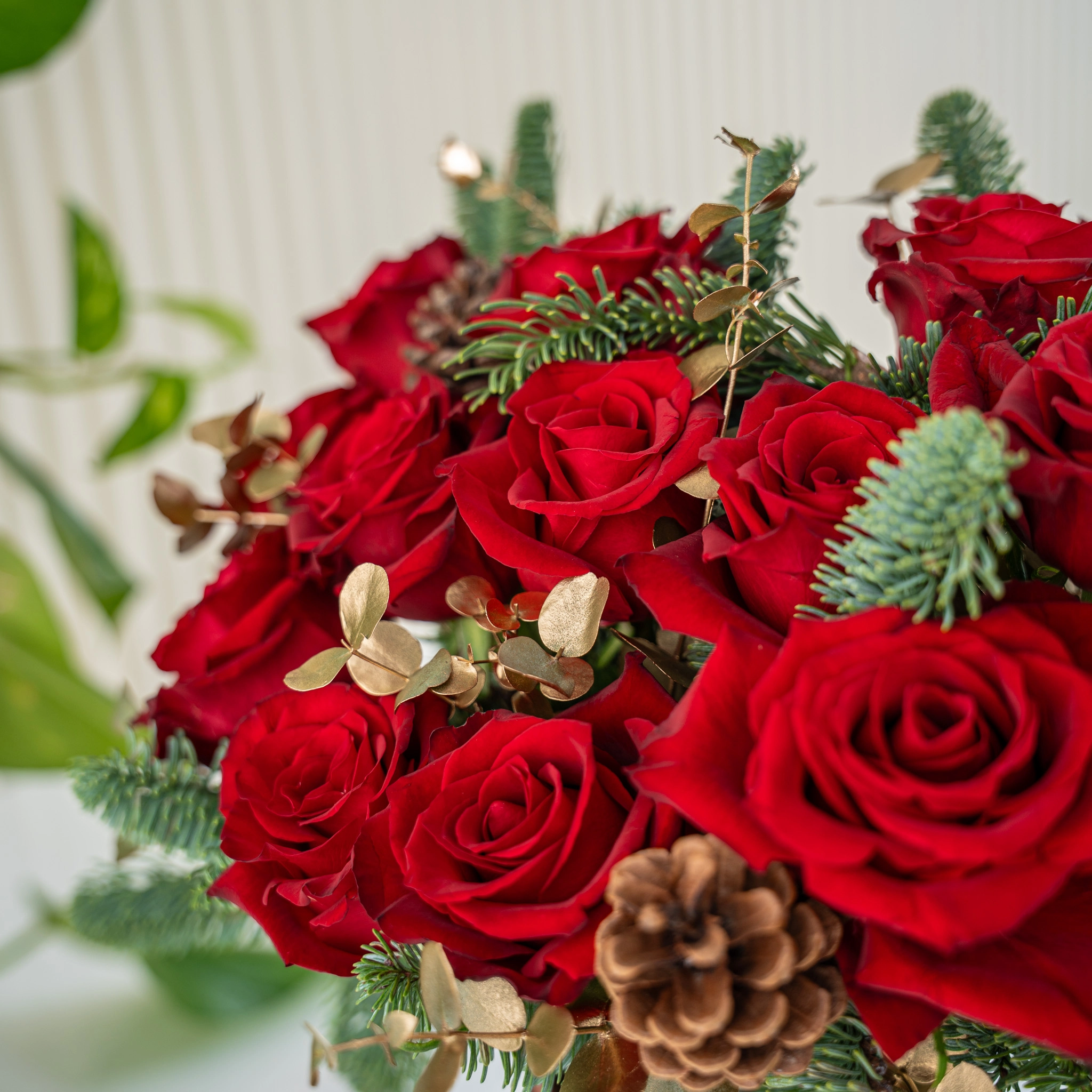 12 red roses with gold-sprayed eucalyptus and nobilis leaves in a glass vase.