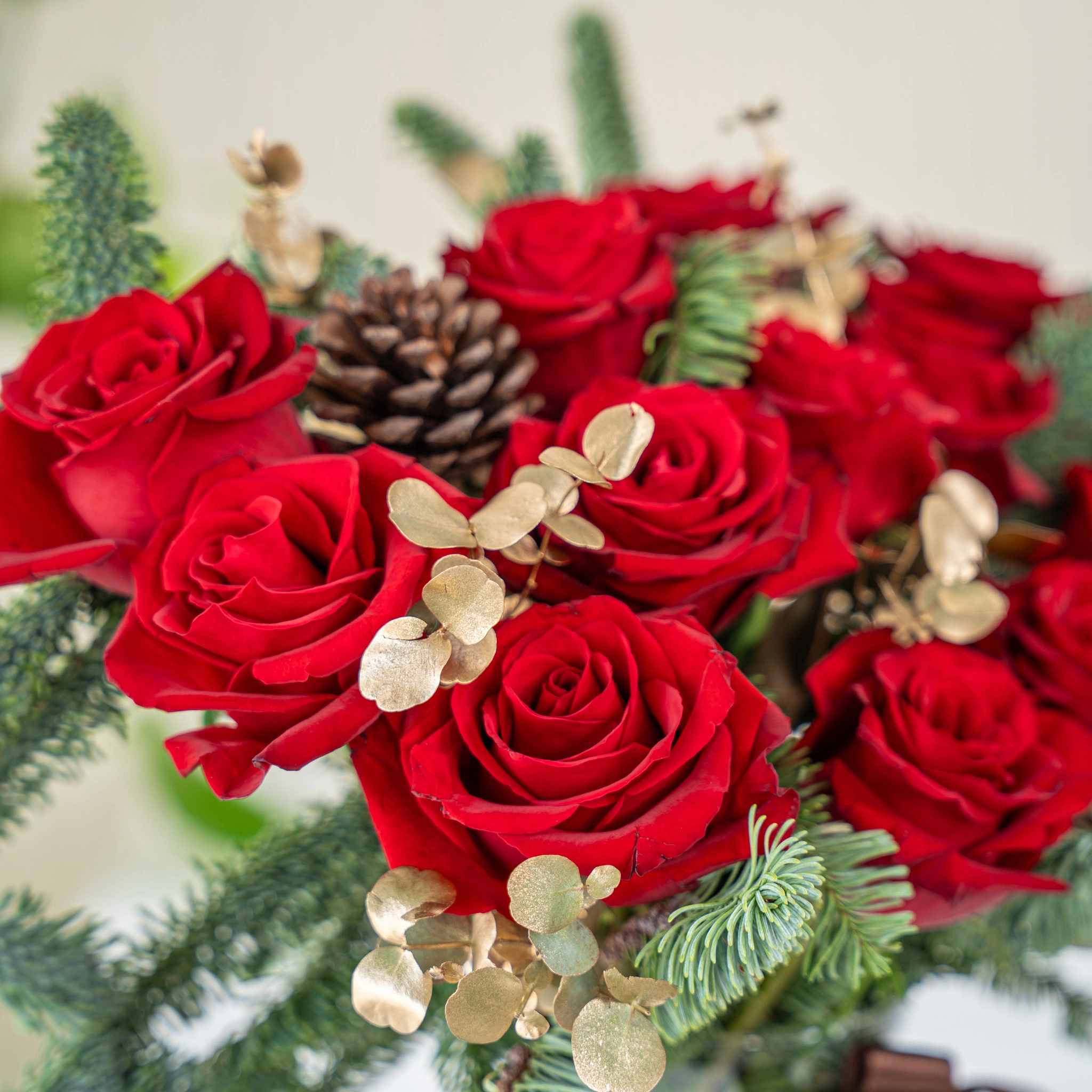 12 red roses with gold-sprayed eucalyptus and nobilis leaves in a glass vase.