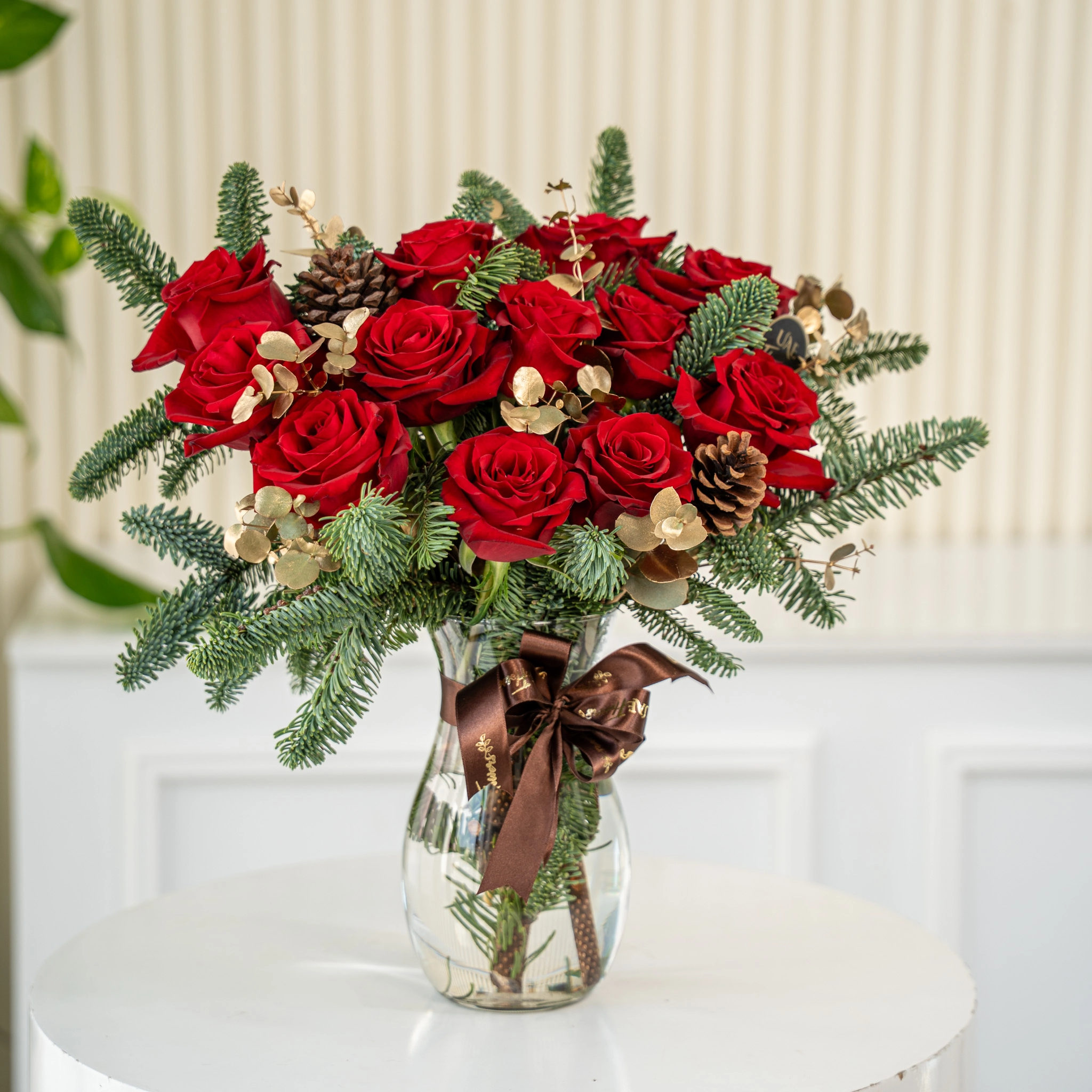 12 red roses with gold-sprayed eucalyptus and nobilis leaves in a glass vase.