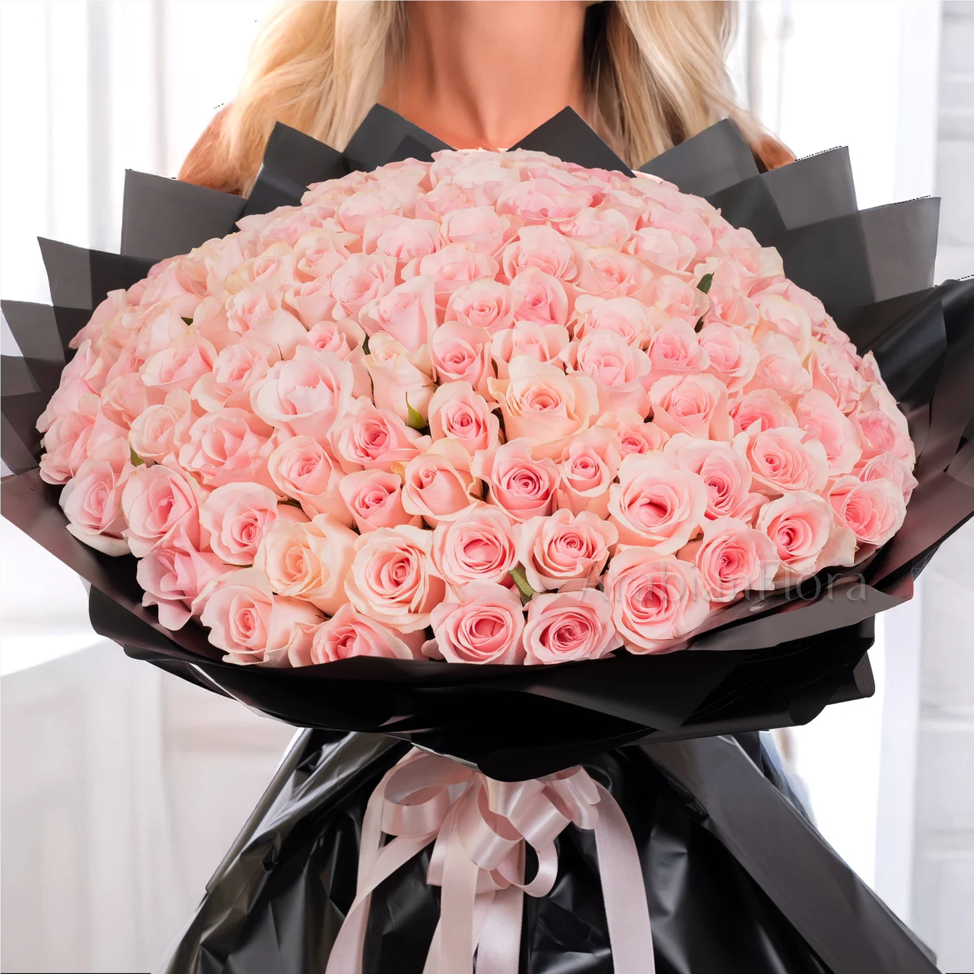 Bouquet of 100 pink roses in black paper packing tied with pink ribbons.