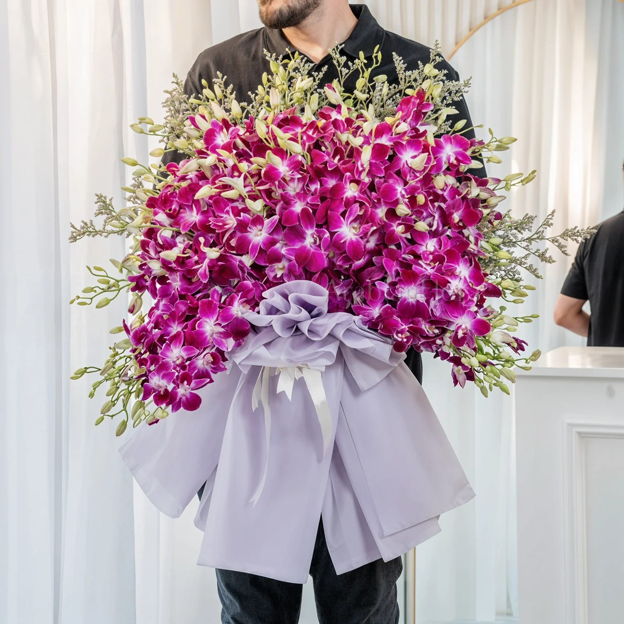 Bouquet of 80 purple orchids in paper packing tied with ribbons.