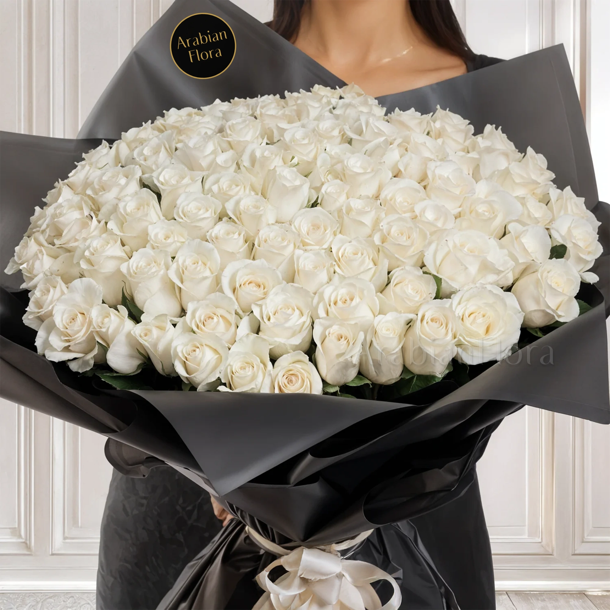 Bouquet of 100 white roses in black paper packing tied with ribbons.