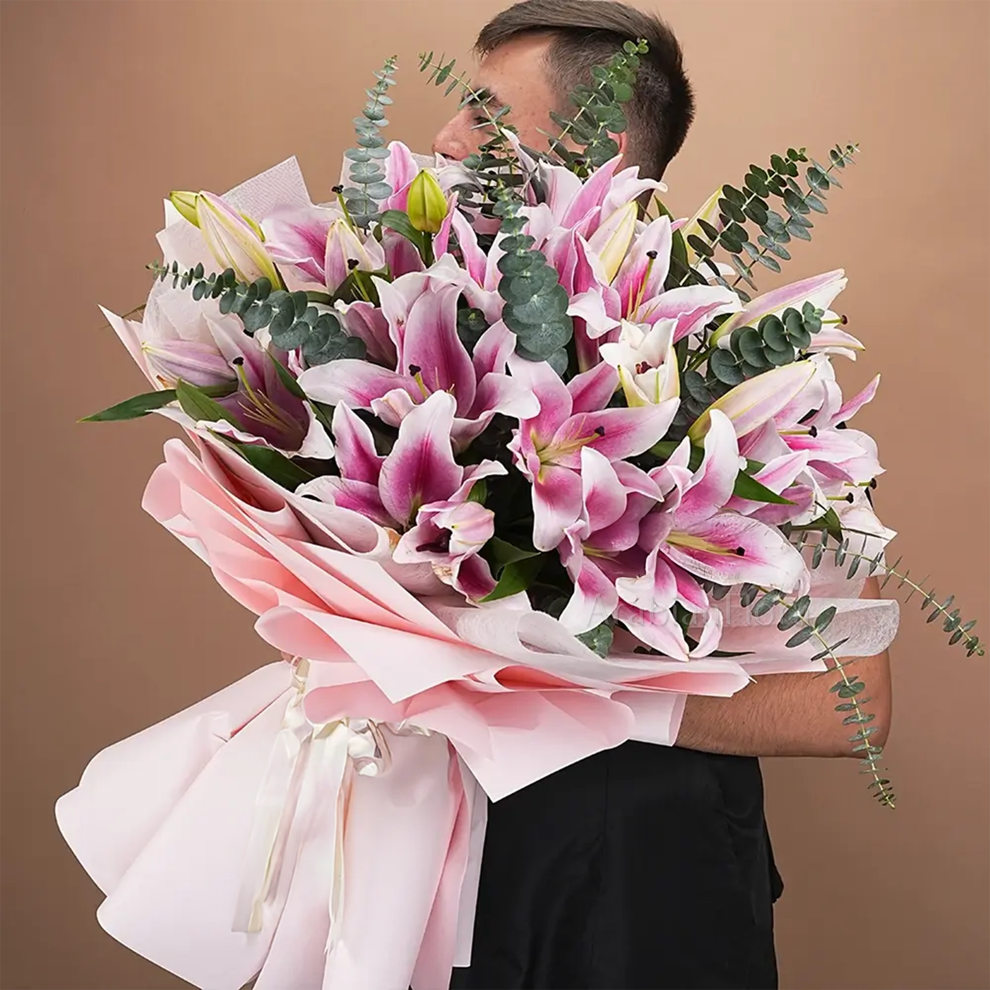 Bouquet of 10 pink lilies with eucalyptus leaf and green fillers in pink wrapping paper tied with pink ribbon.
