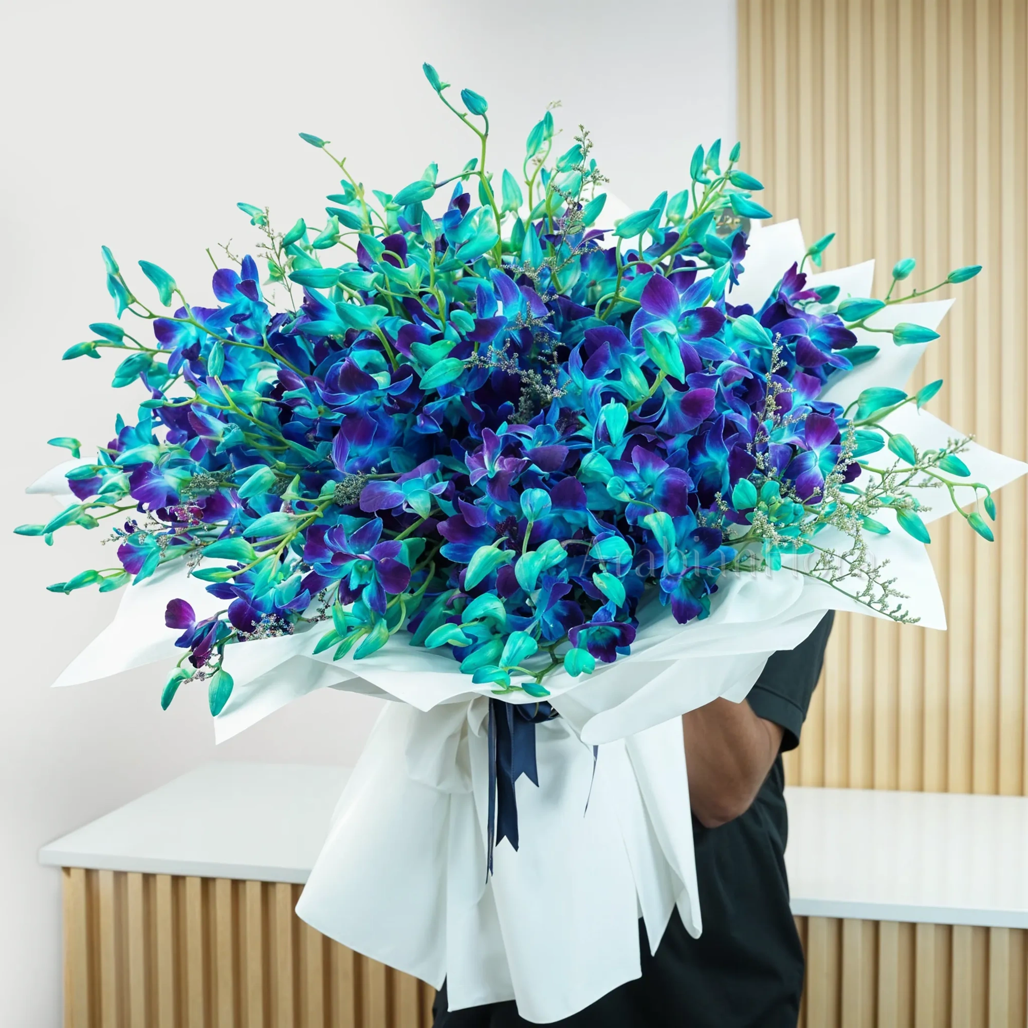 Bouquet of 80 blue orchids with fillers in white wrapping paper tied with blue ribbons.