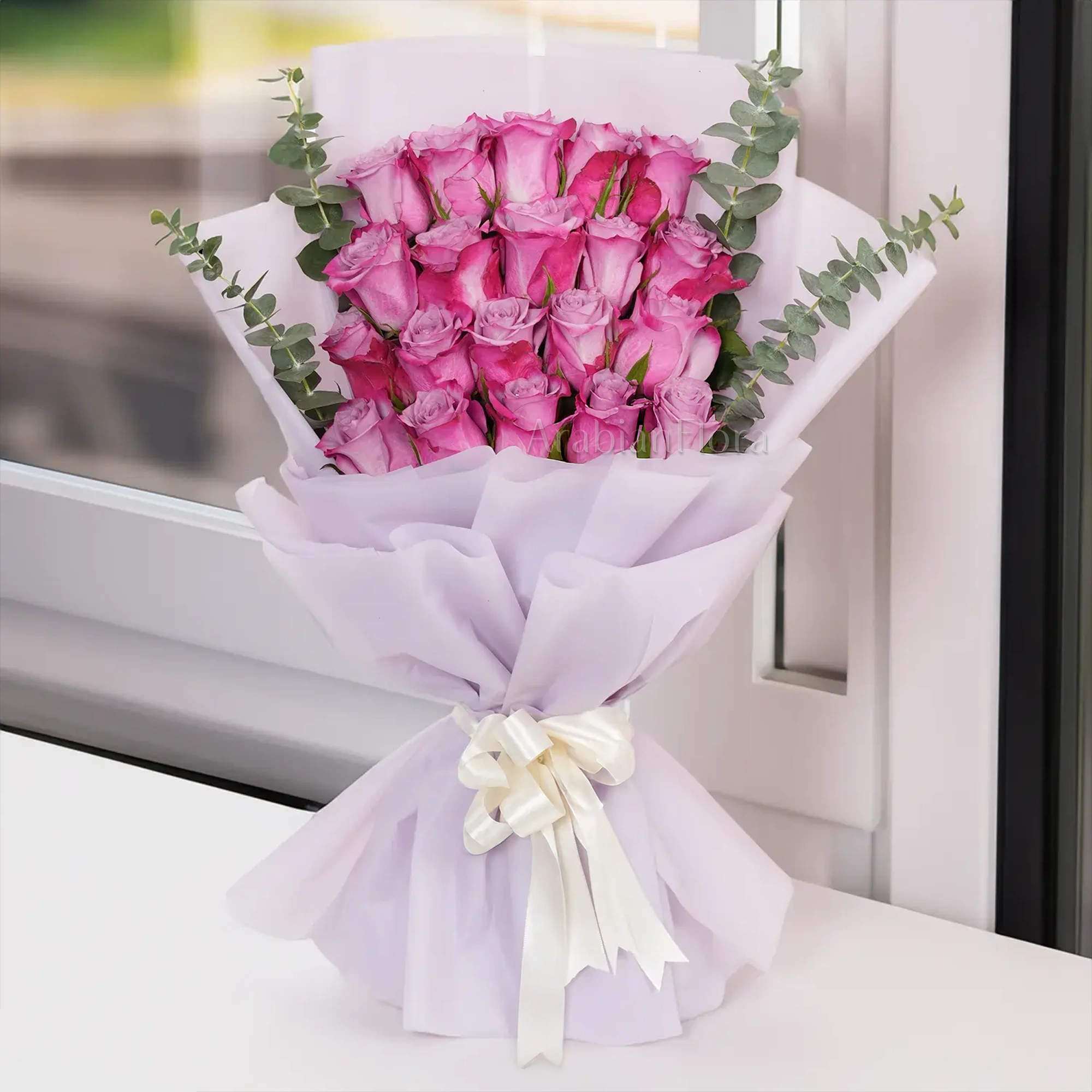 Bouquet of 20 purple roses with eucalyptus leaf in pink paper packing tied with white ribbons.