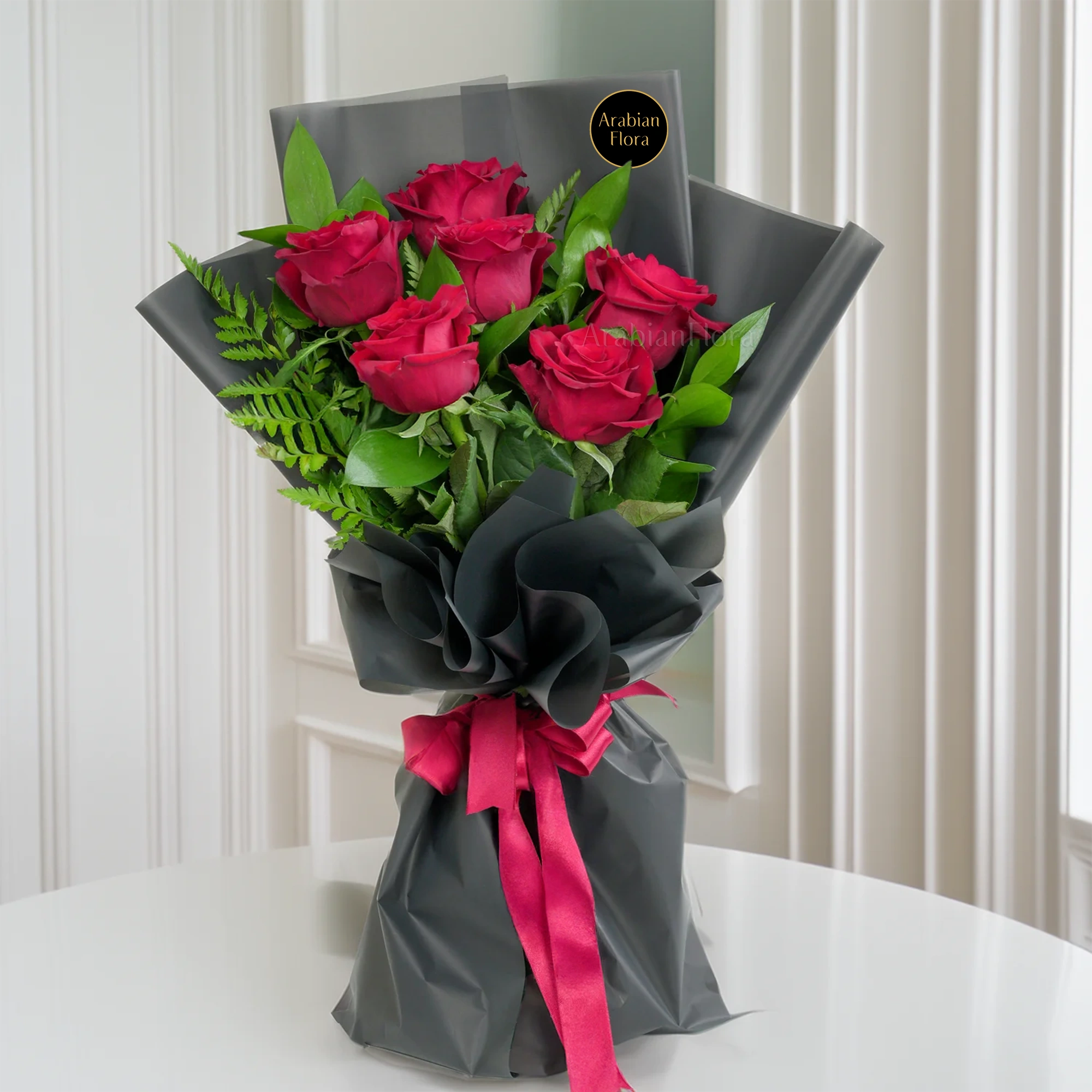 Bouquet of 6 red roses with green fillers in black paper packing tied with ribbons.