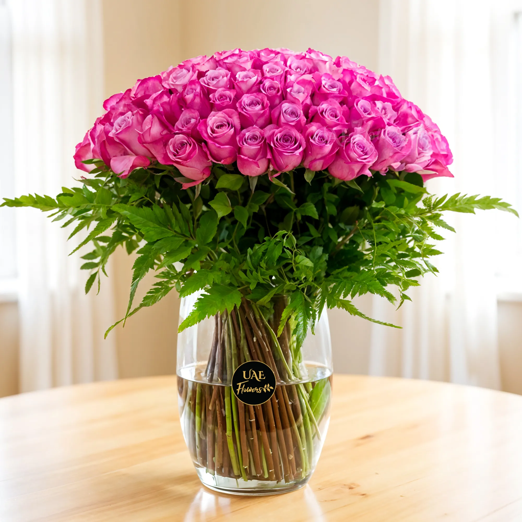 100 Purple Roses with green fillers in a glass vase.