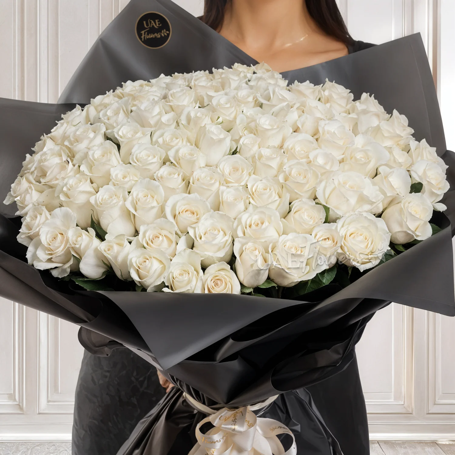 Bouquet of 100 white roses in black paper packing tied with ribbons.