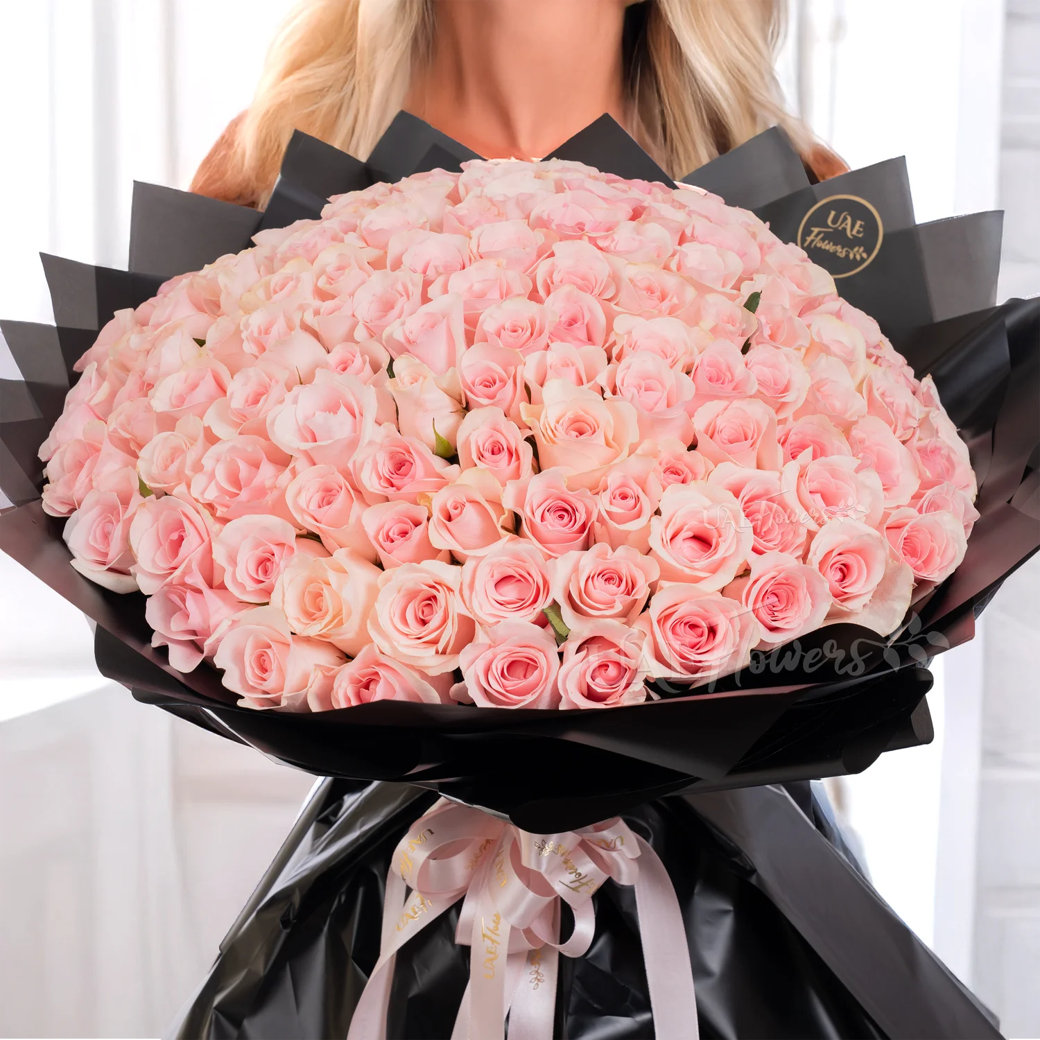 Bouquet of 100 pink roses in black paper packing tied with pink ribbons.