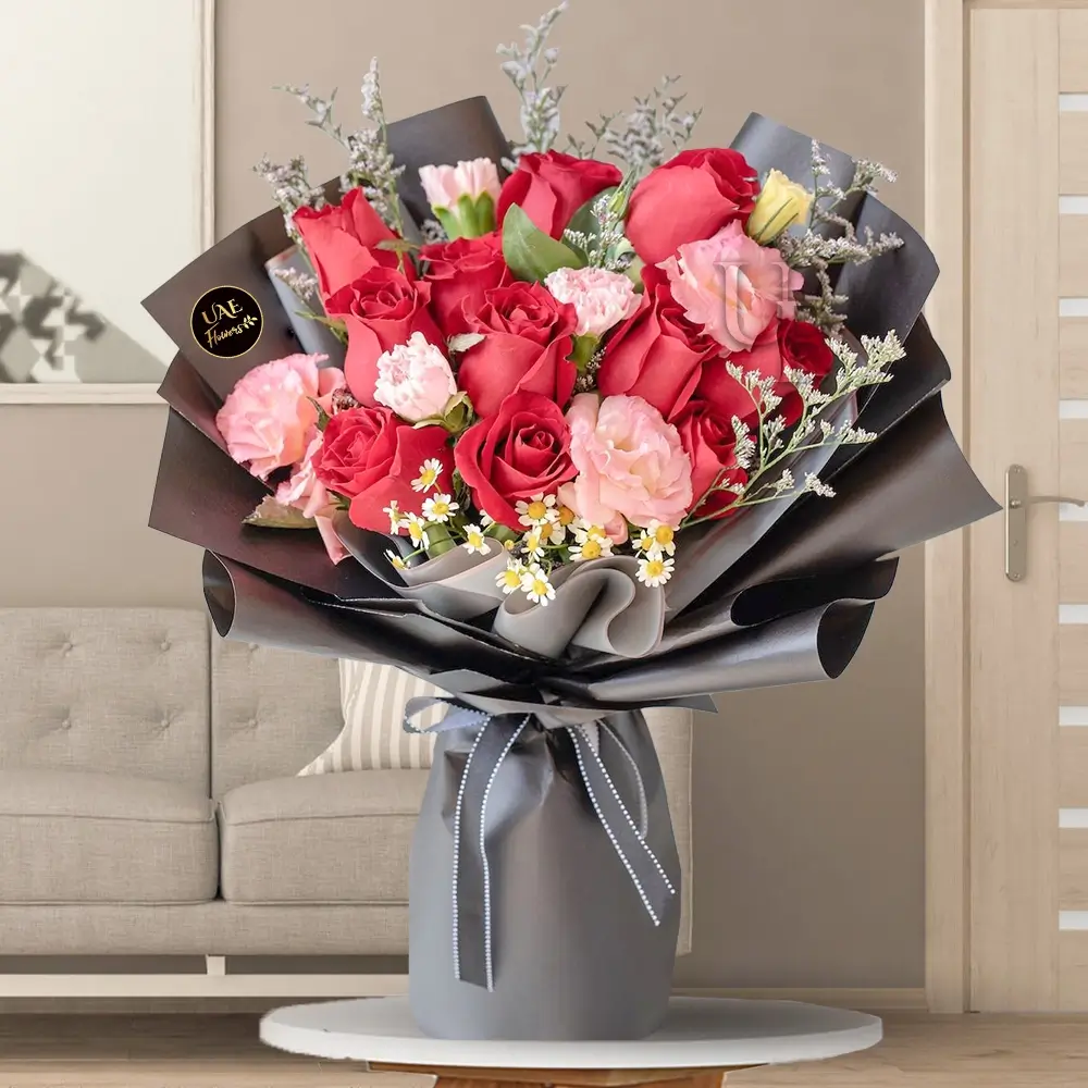 Bouquet of 12 stems of red roses and 6 stems of pink carnations with fillers in black wrapping.