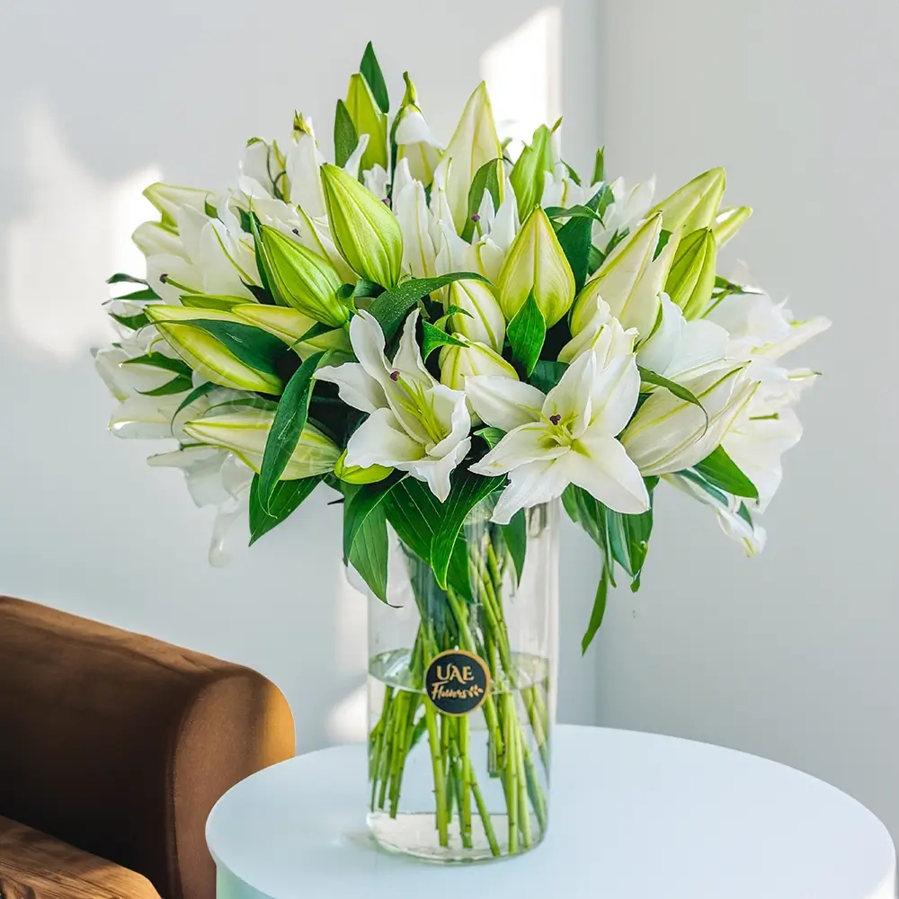 15 stems of white lilies with green fillers in a glass vase.