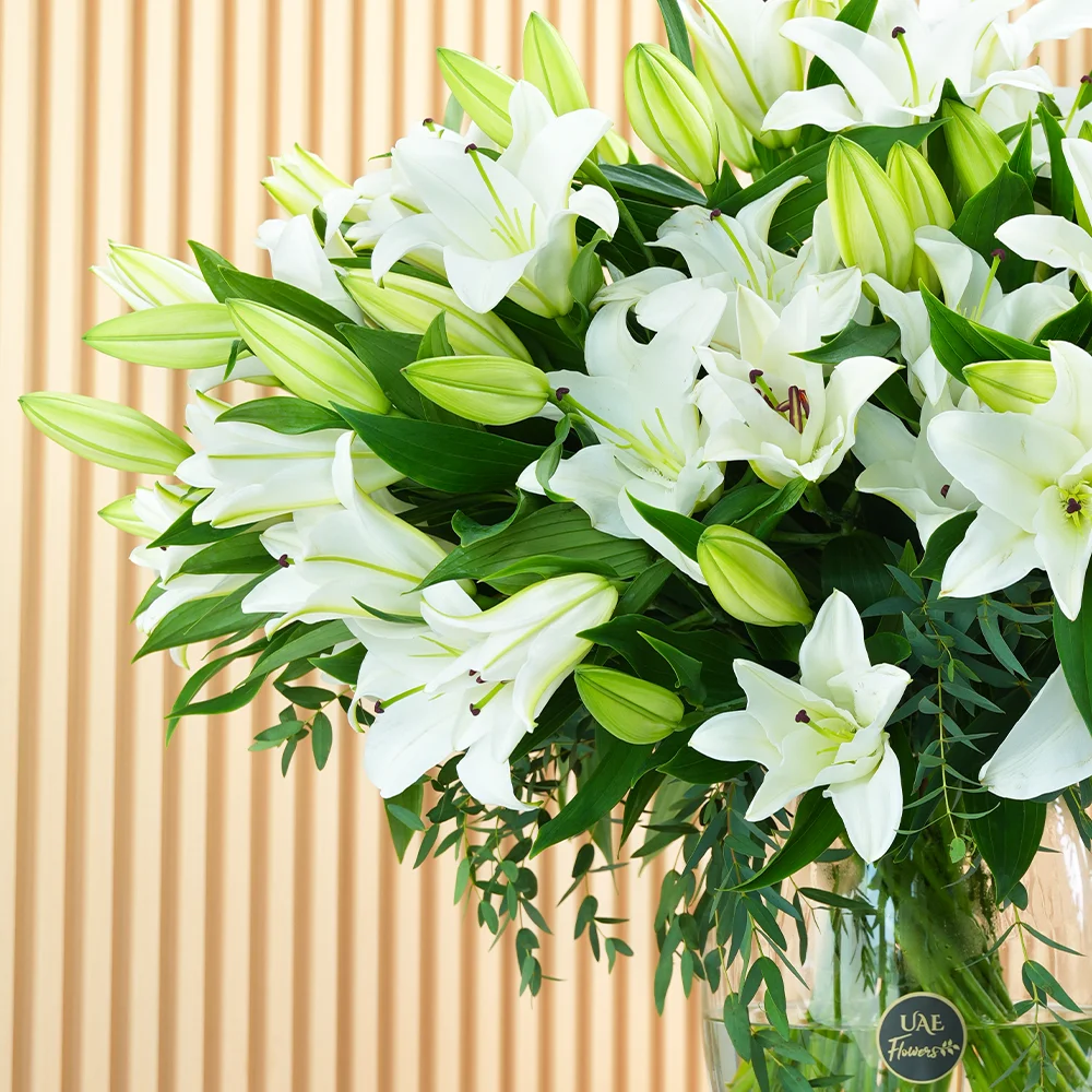 An arrangement of 20 white lilies with green fillers in a glass vase.