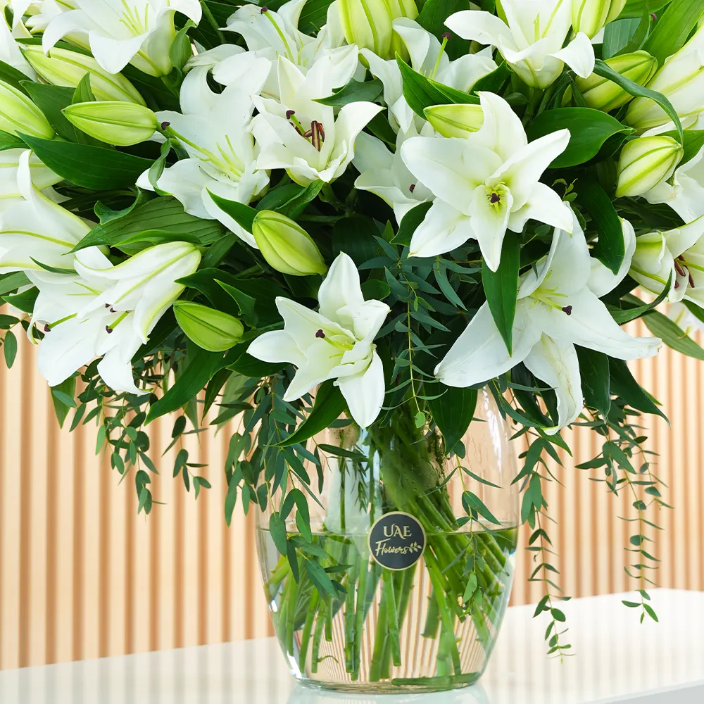 An arrangement of 20 white lilies with green fillers in a glass vase.