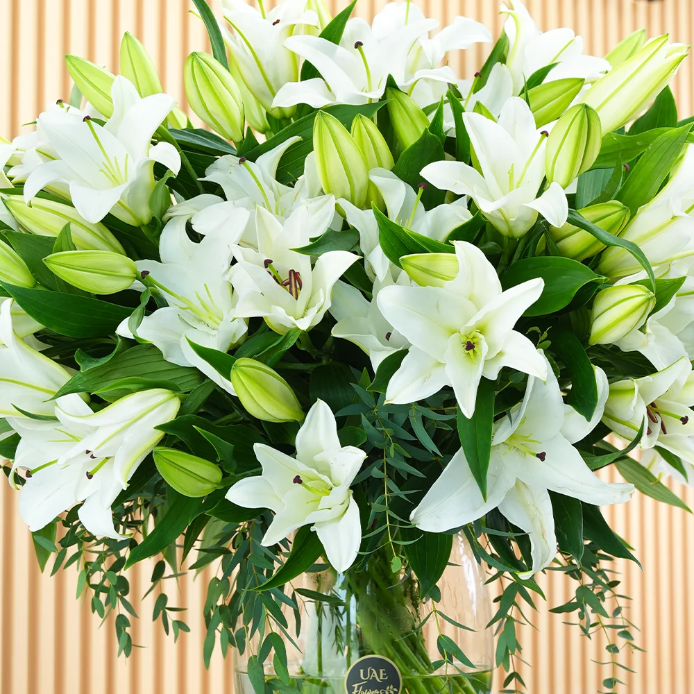 An arrangement of 20 white lilies with green fillers in a glass vase.