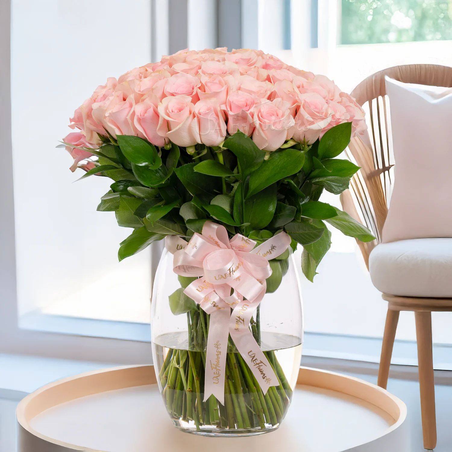 A glass vase arrangement of 50 pink roses with  with pink ribbons.