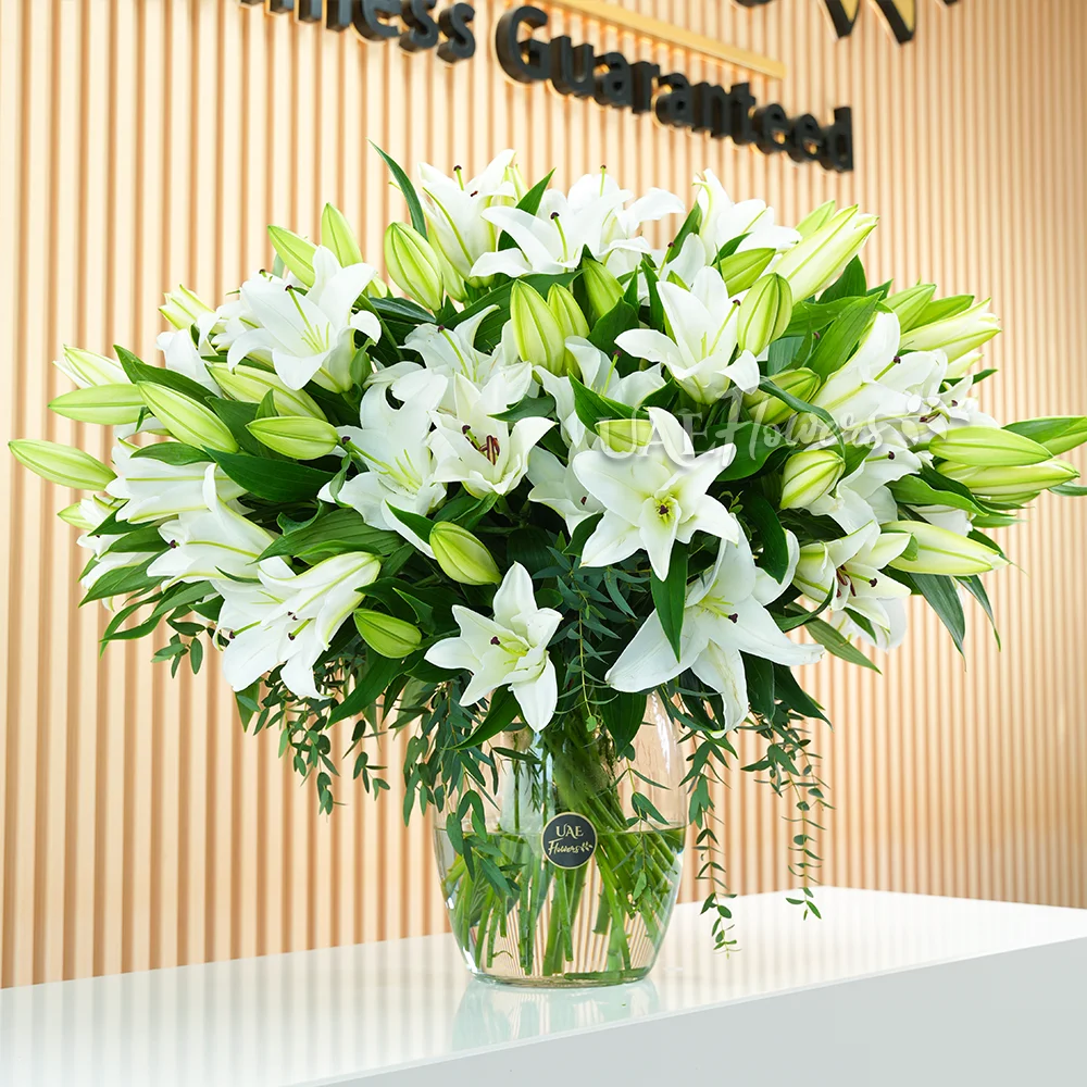 An arrangement of 20 white lilies with green fillers in a glass vase.