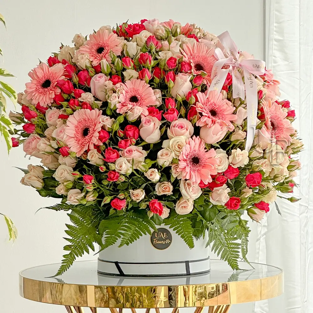 HALF round Arrangement of 20 stems of pink gerberas, 20 stems of pink roses, 20 stems of pink spray roses and 20 stems of peach spray roses with green fillers and eucalyptus leaf in a white round box.