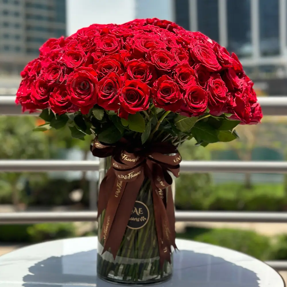 100 stems of red roses with green fillers in a glass vase beautifully tied with ribbons.