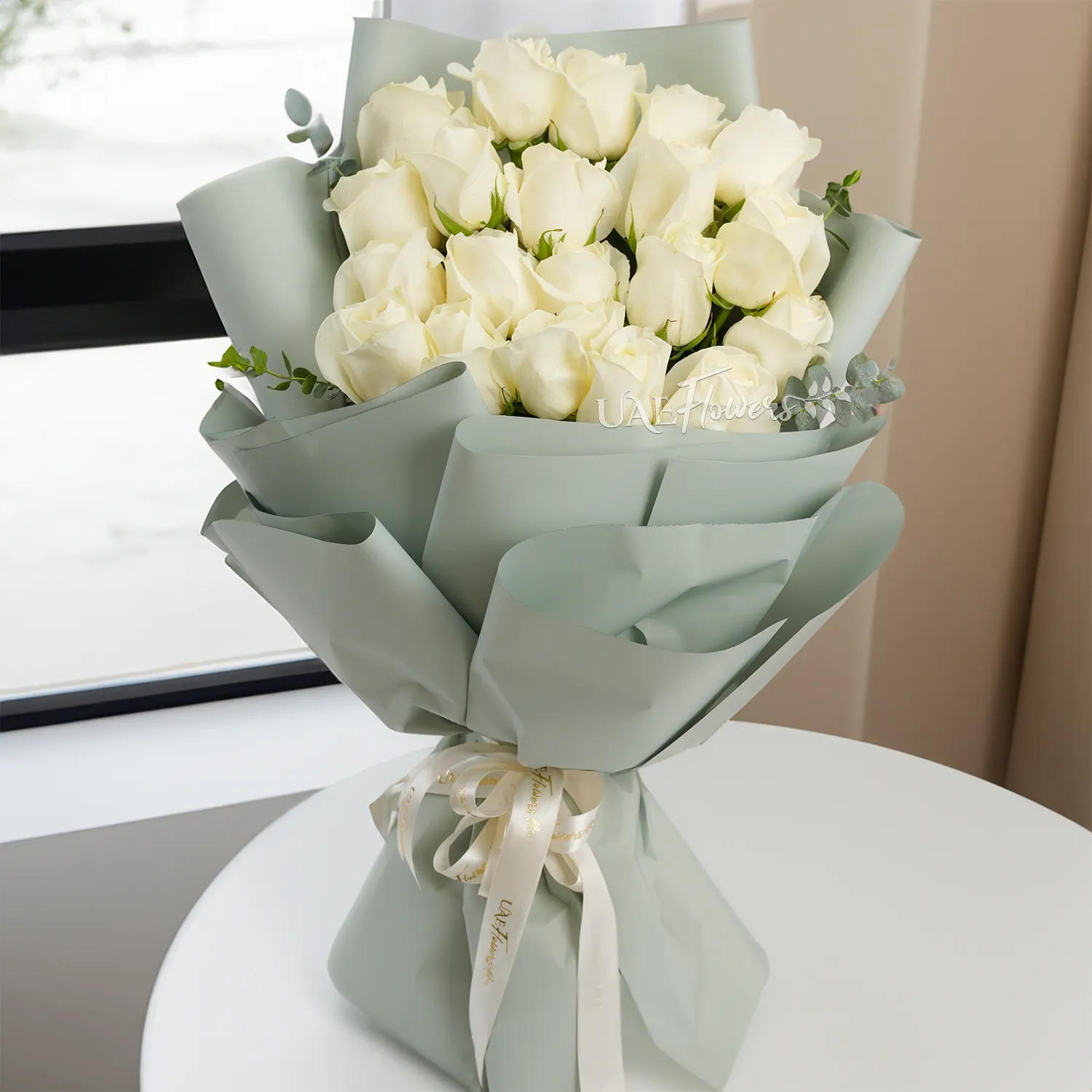 Bouquet of 20 white roses with green fillers in paper packing tied with white ribbons