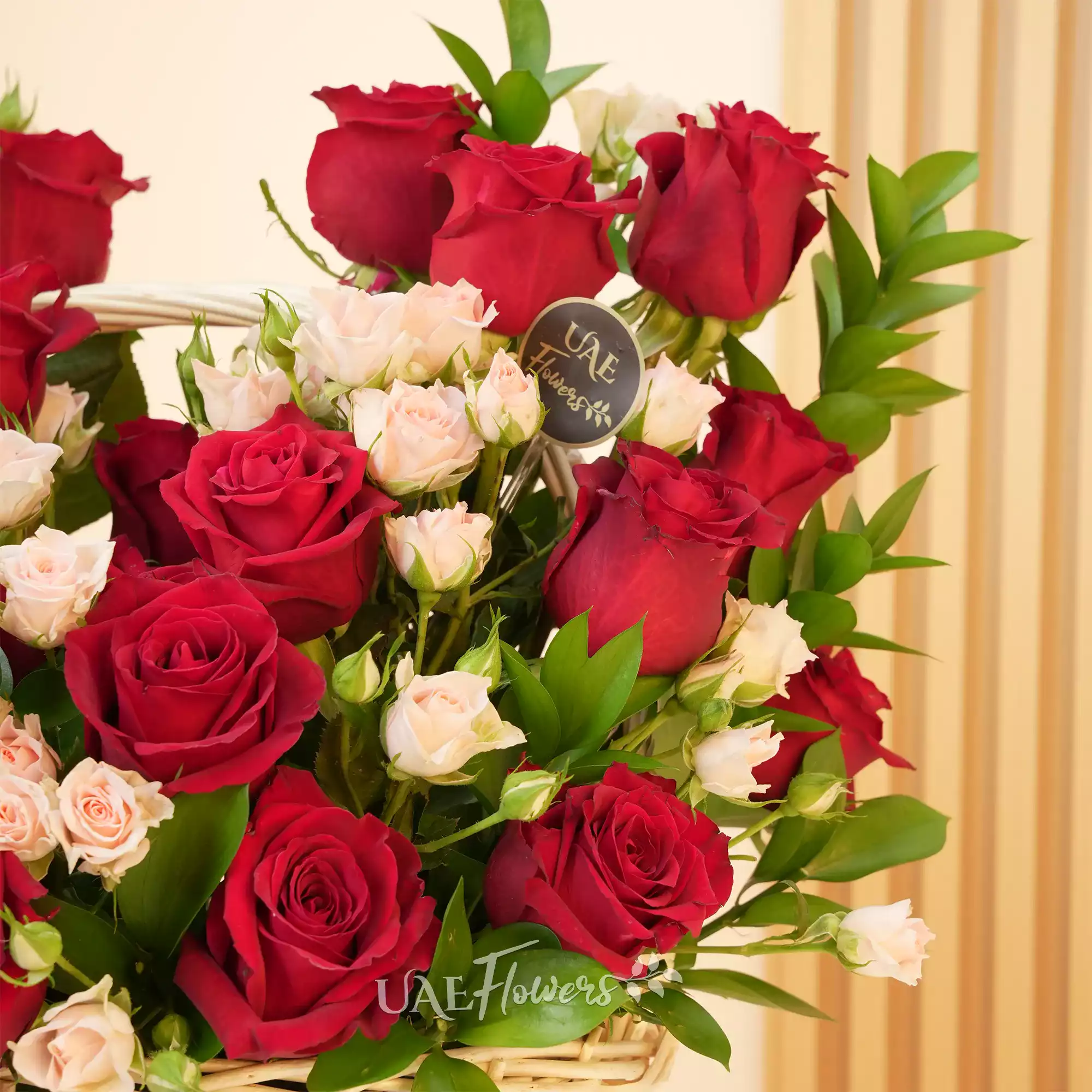An arrangement of 20 red roses and 6 pink spray roses with green fillers in a handle basket.