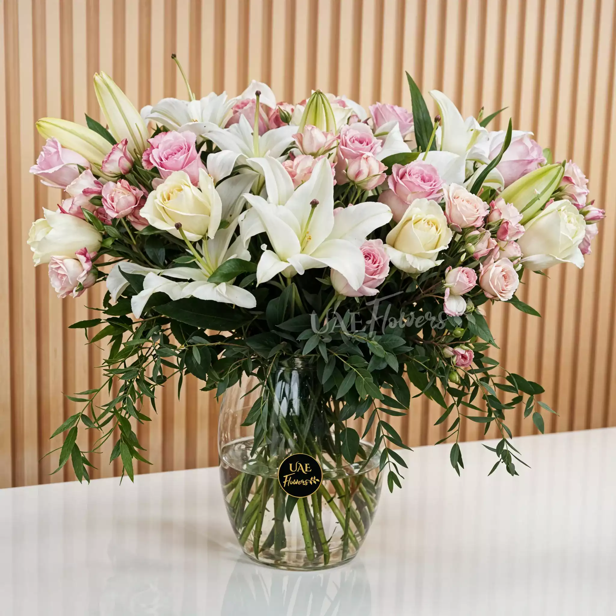 white lilies, white roses, pink roses, pink spray roses with green fillers in a glass vase.
