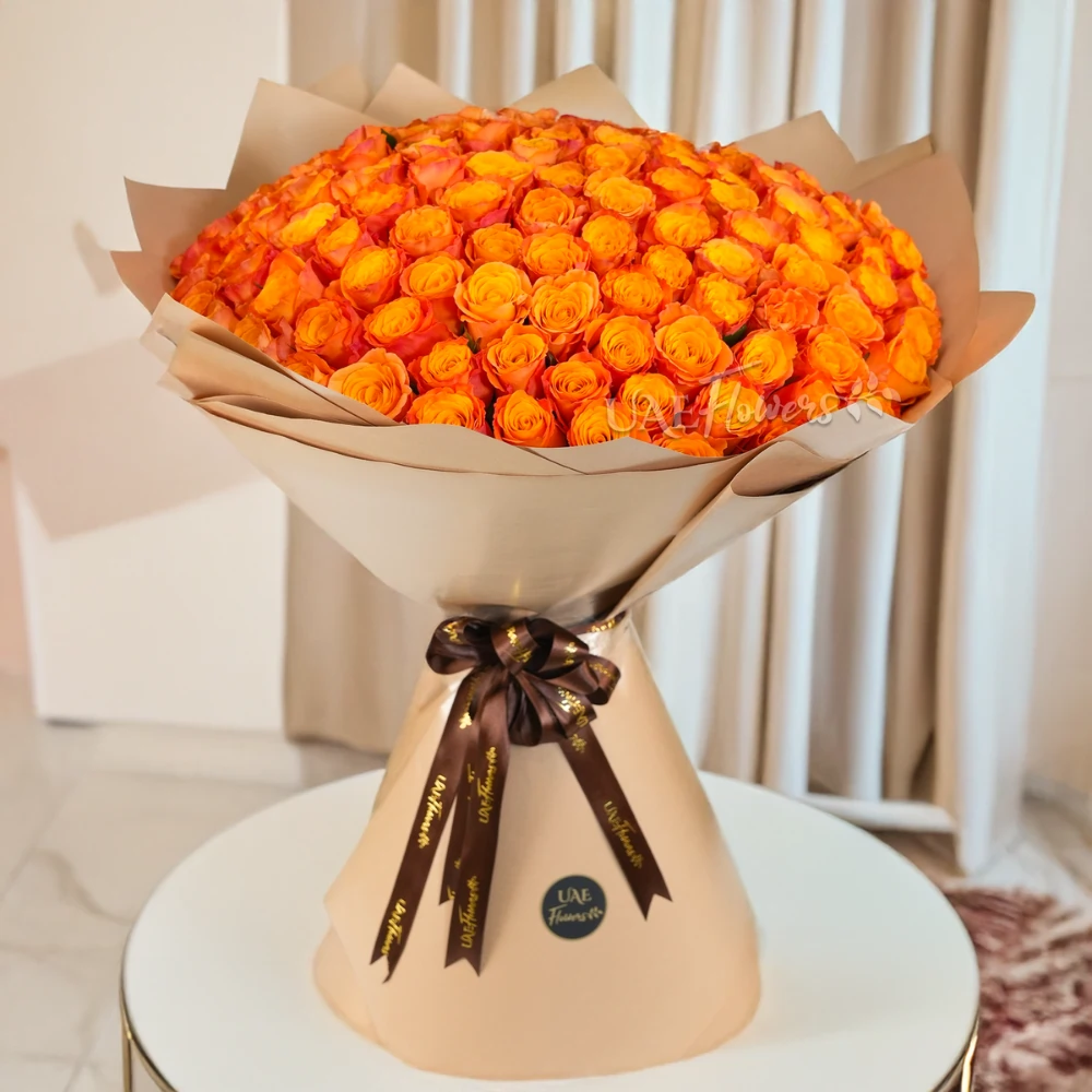 Bouquet of 100 orange roses wrapped in brown paper packing and tied with ribbons.