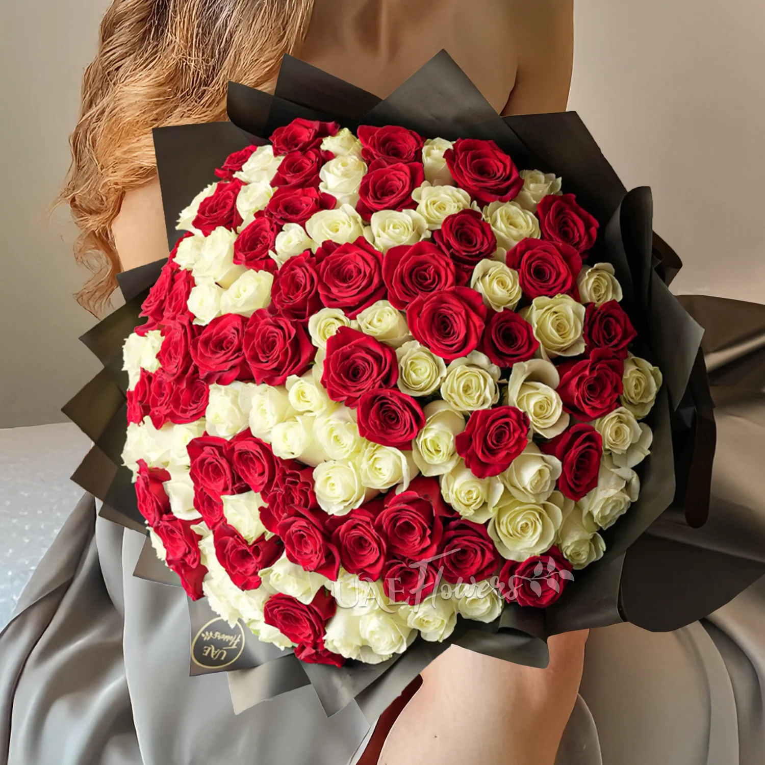Bouquet of 100 red and white roses in black paper packing tied with ribbons.