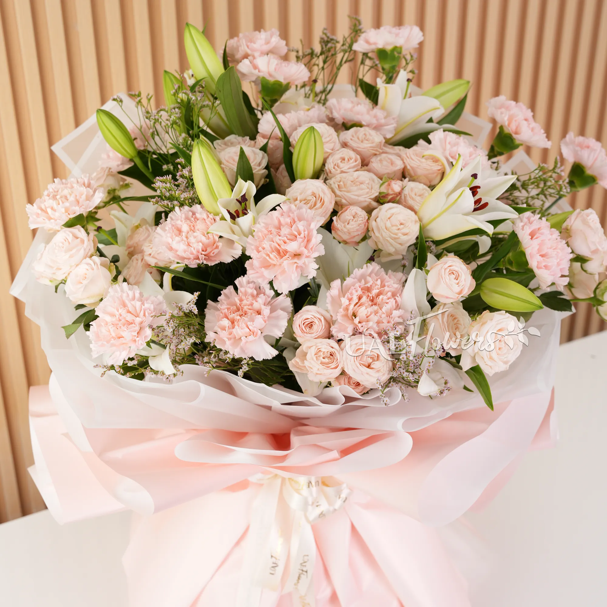 Bouquet of, white lilies, pink carnations, pink spray roses with green fillers wrapped in paper packing and tied with ribbons.