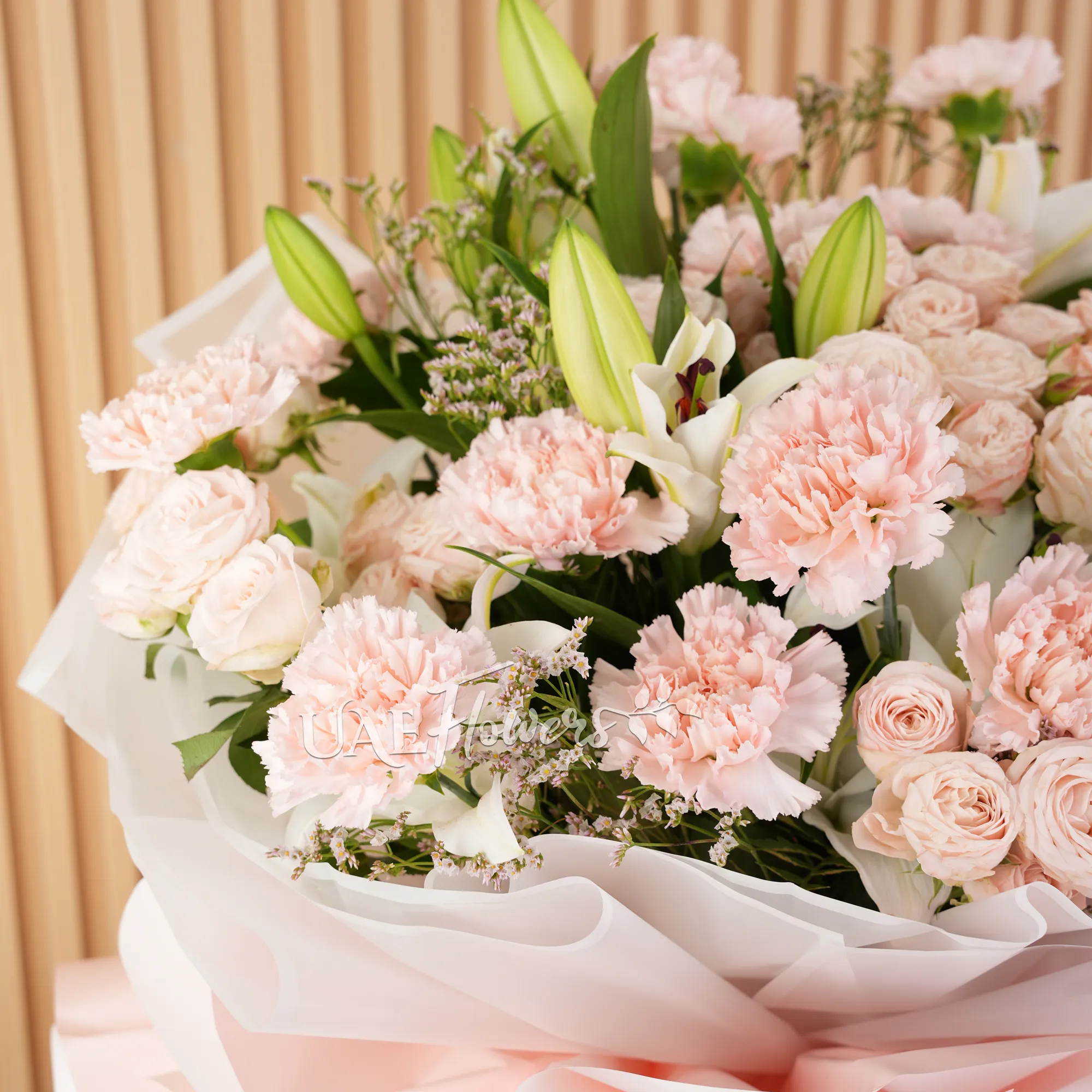 Bouquet of, white lilies, pink carnations, pink spray roses with green fillers wrapped in paper packing and tied with ribbons.