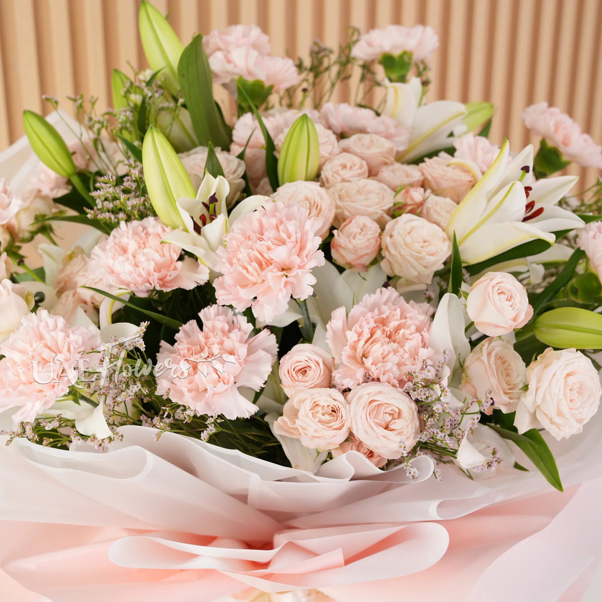 Bouquet of, white lilies, pink carnations, pink spray roses with green fillers wrapped in paper packing and tied with ribbons.