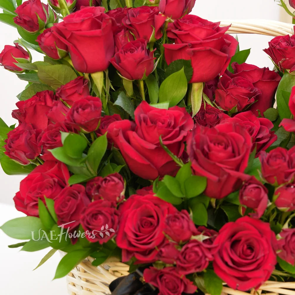 An arrangement of 20 red roses and 5 red spray roses with green fillers in a basket.