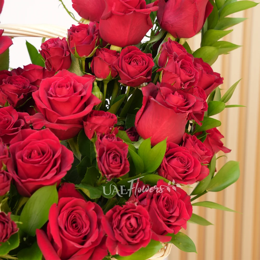 An arrangement of 20 red roses and 5 red spray roses with green fillers in a basket.
