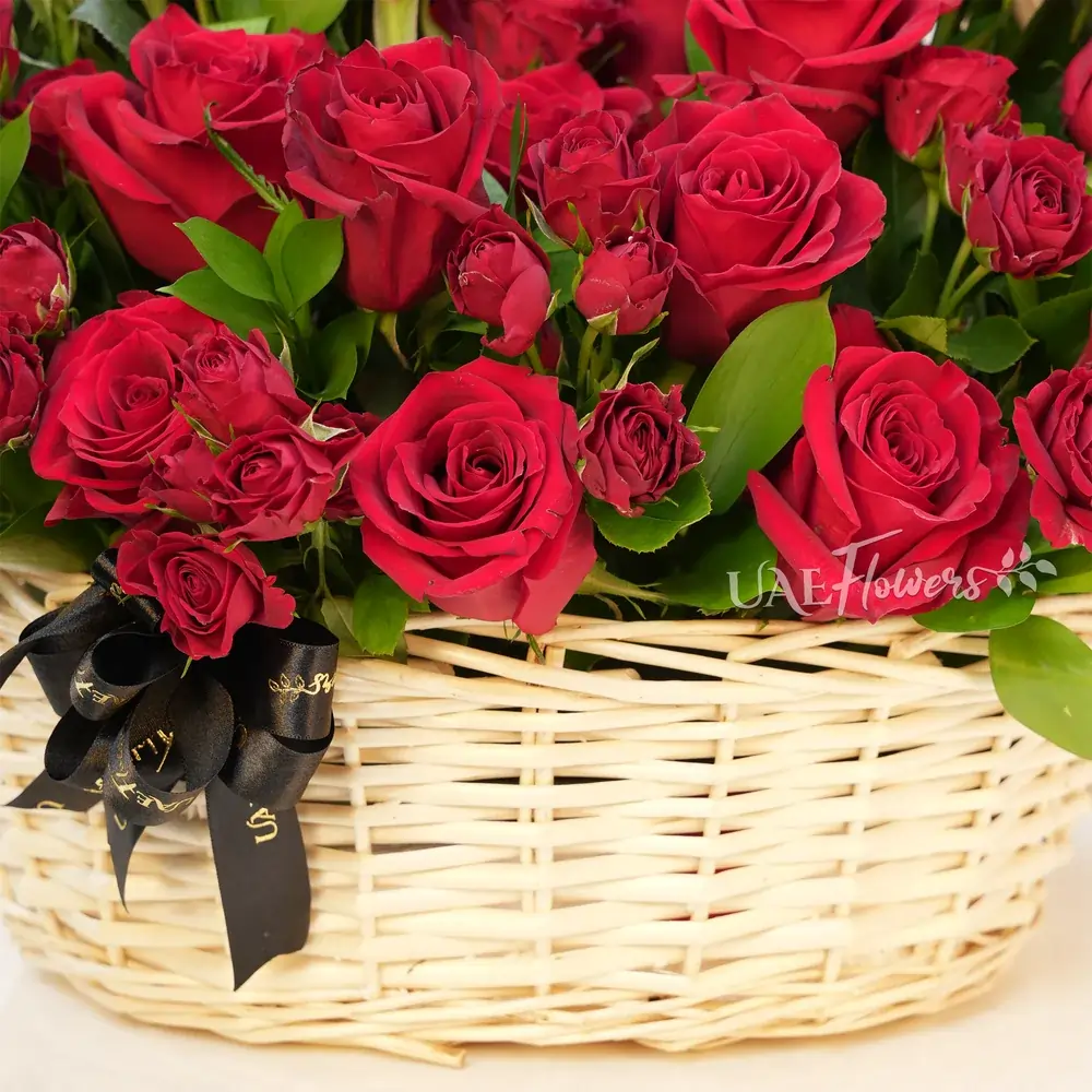 An arrangement of 20 red roses and 5 red spray roses with green fillers in a basket.