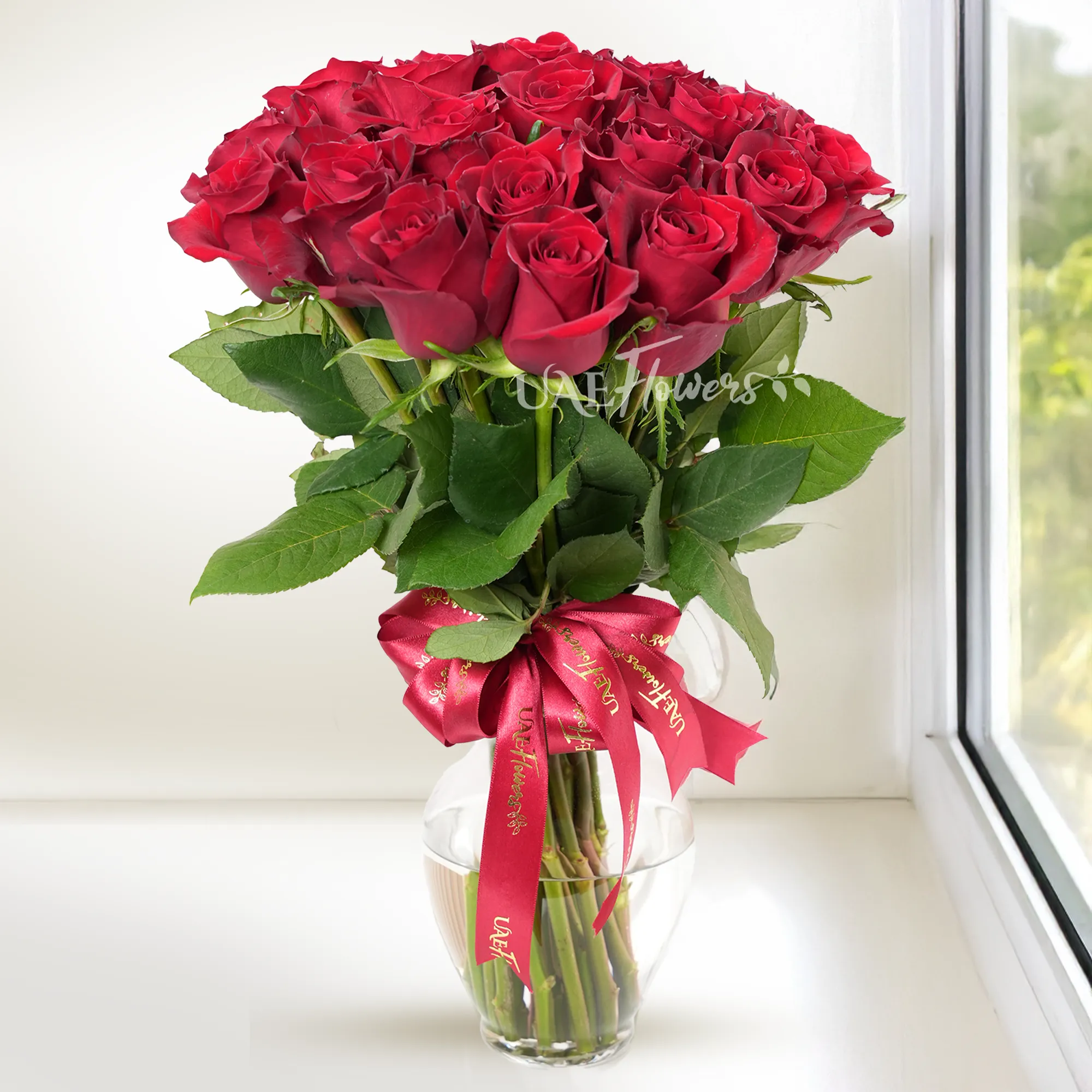 A vase arrangement of 30 red roses with green fillers tied with red ribbons.