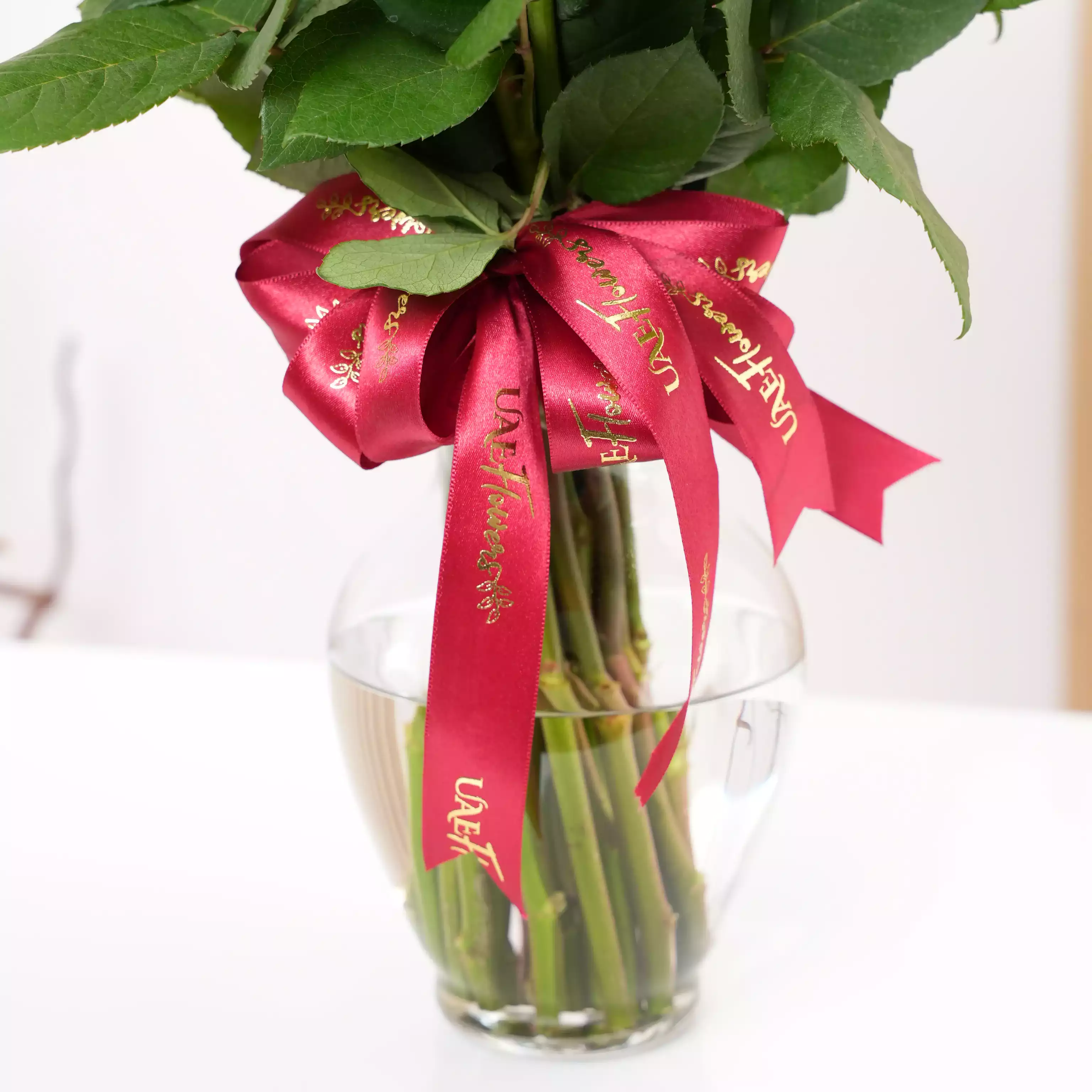 A vase arrangement of 30 red roses with green fillers tied with red ribbons.