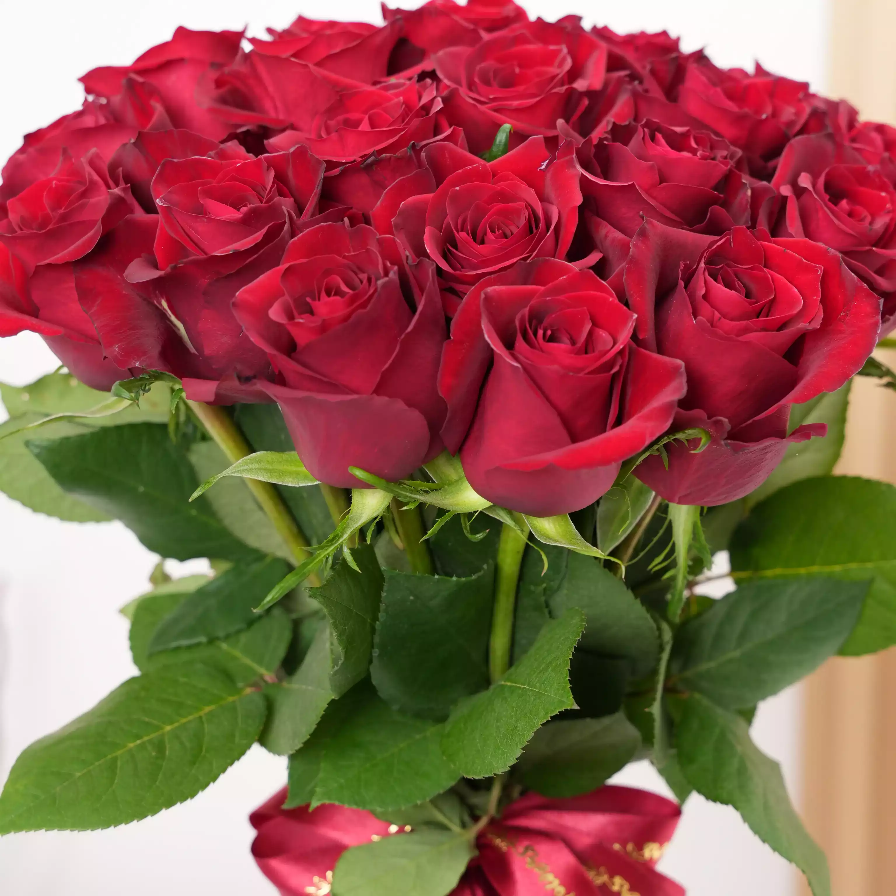 A vase arrangement of 30 red roses with green fillers tied with red ribbons.