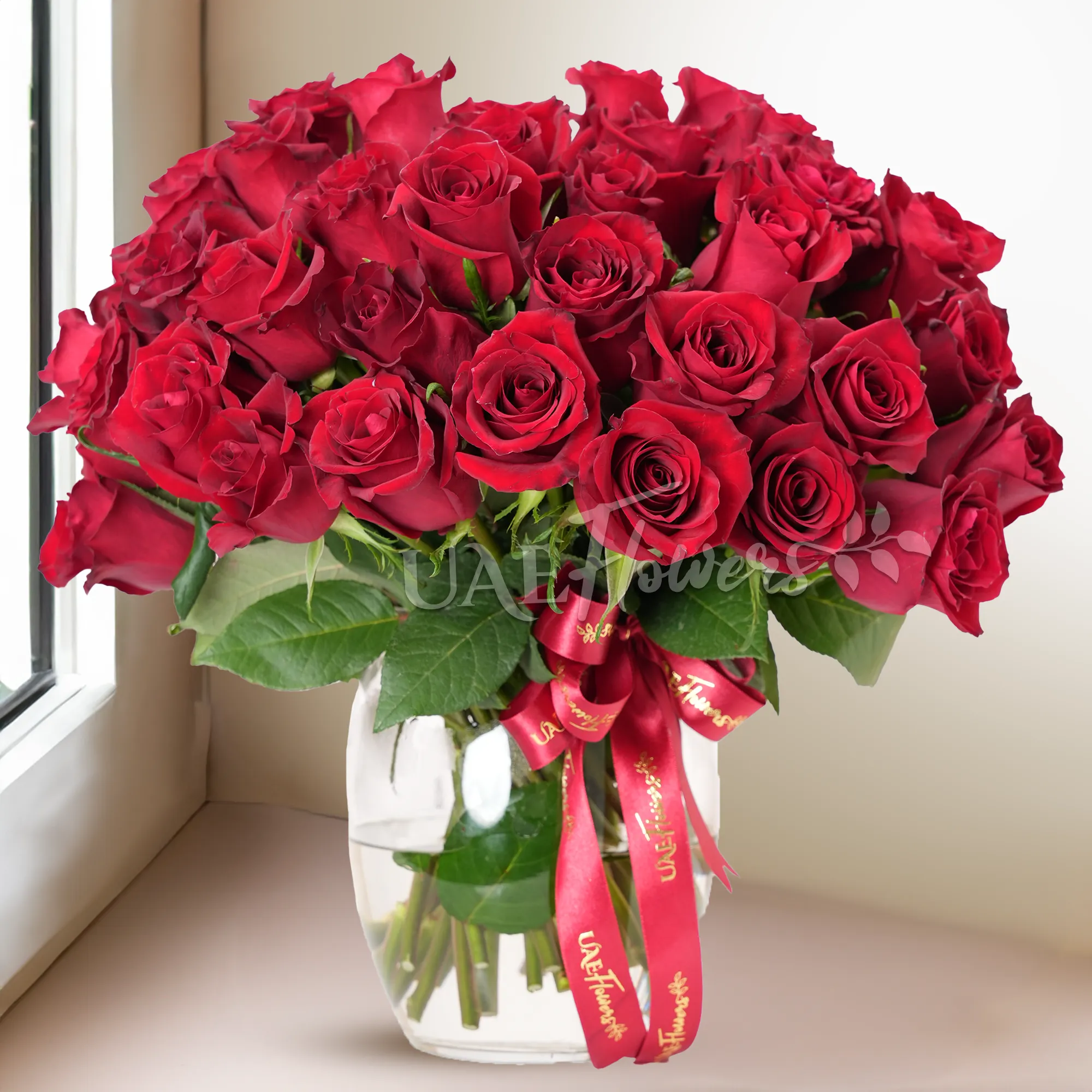 A vase arrangement of 40 red roses with green fillers and tied with red ribbons.