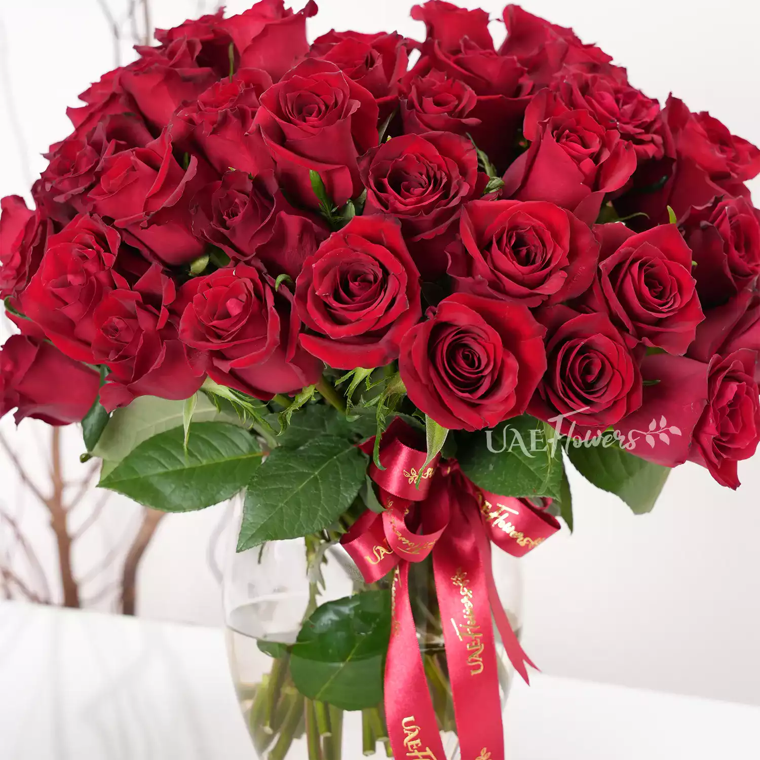 A vase arrangement of 40 red roses with green fillers and tied with red ribbons.