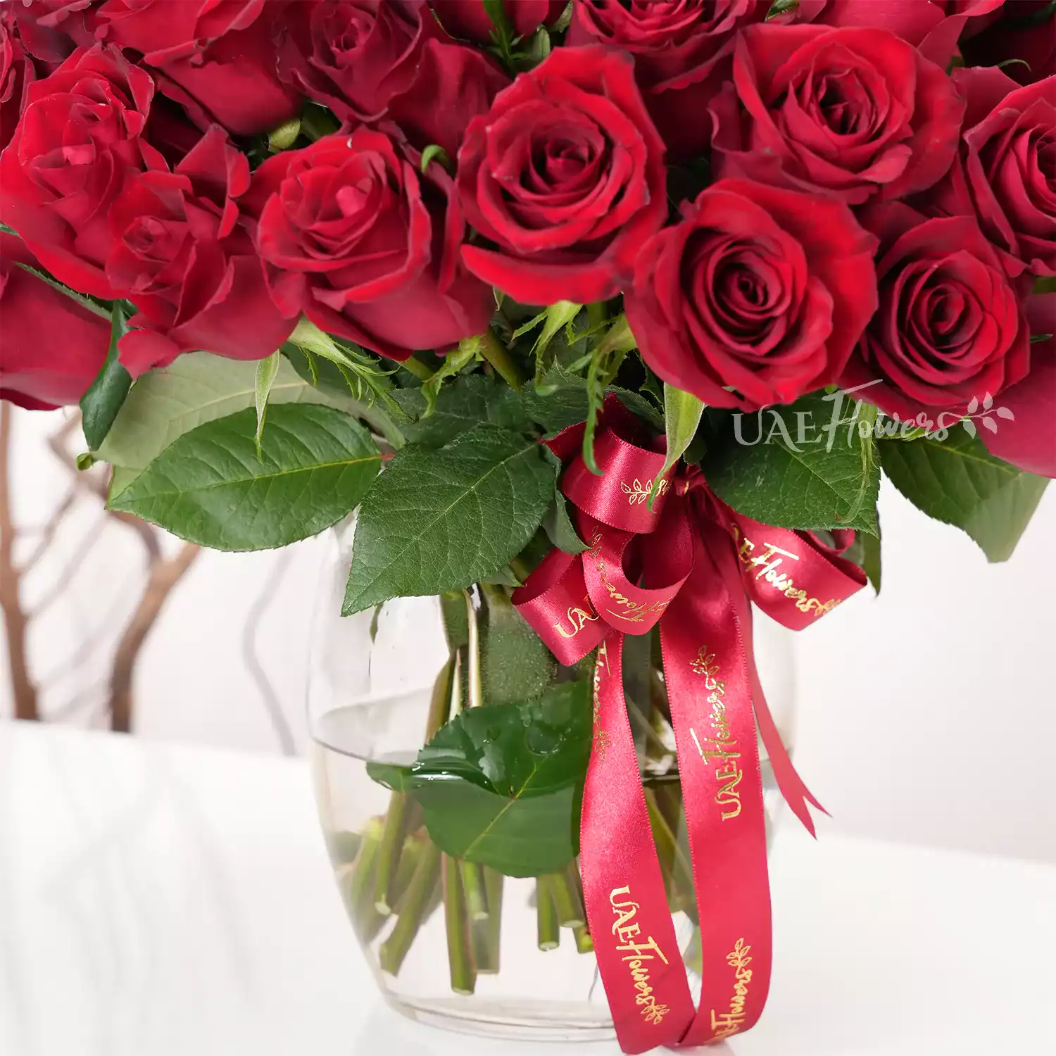 A vase arrangement of 40 red roses with green fillers and tied with red ribbons.