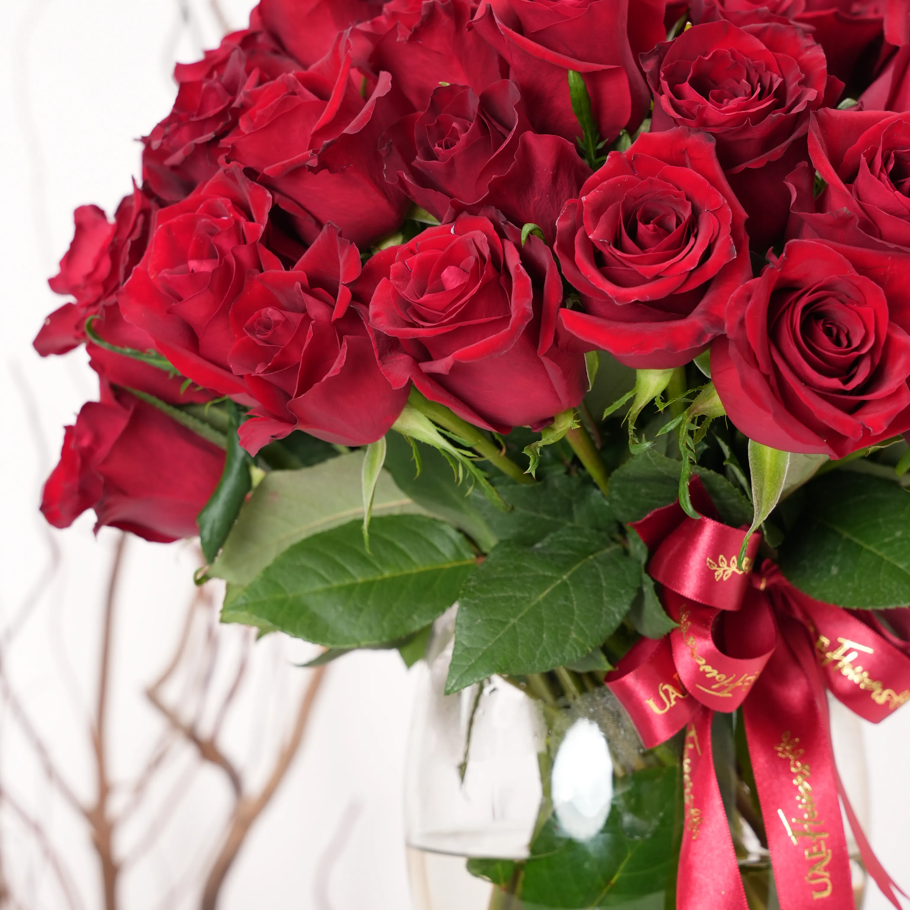 A vase arrangement of 40 red roses with green fillers and tied with red ribbons.