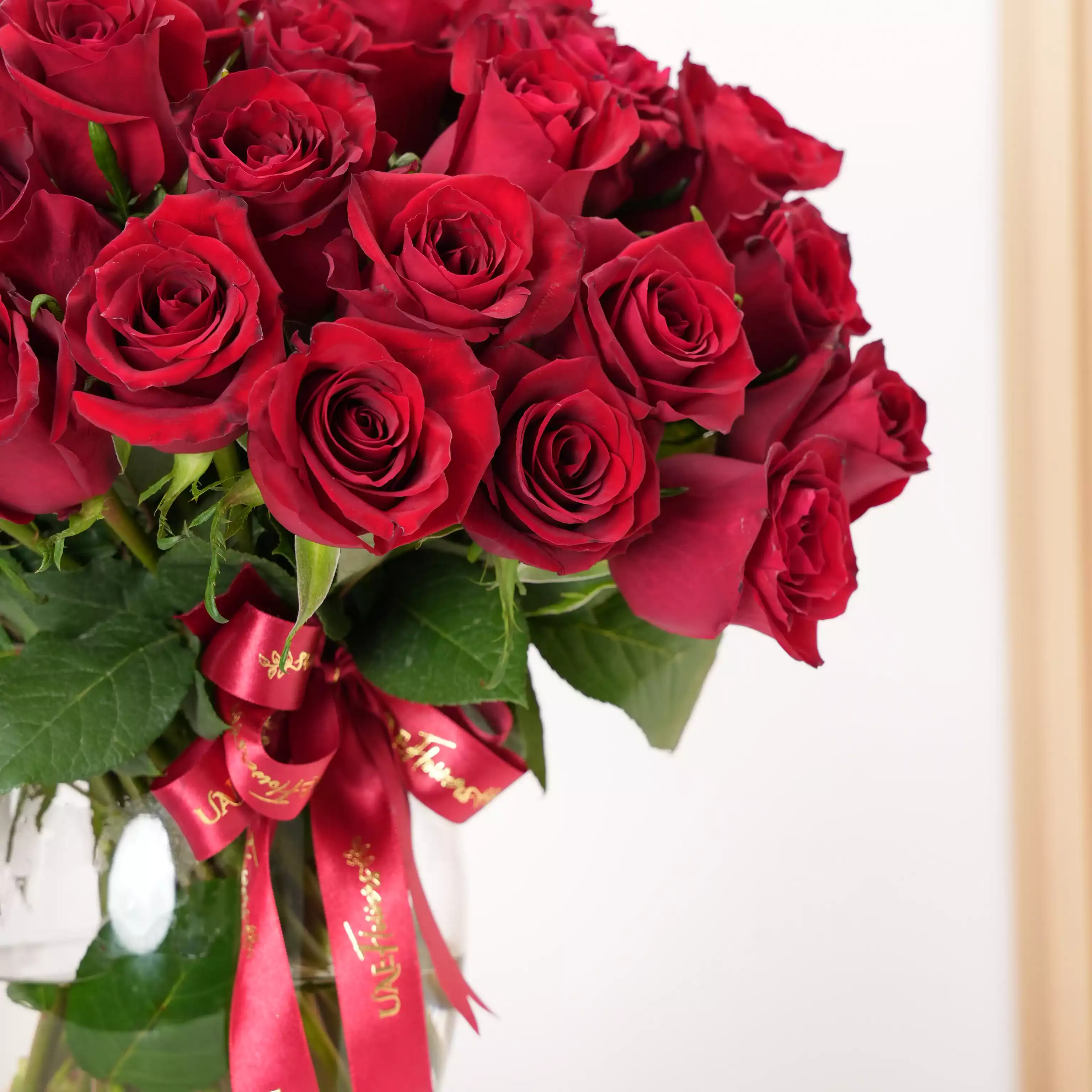 A vase arrangement of 40 red roses with green fillers and tied with red ribbons.