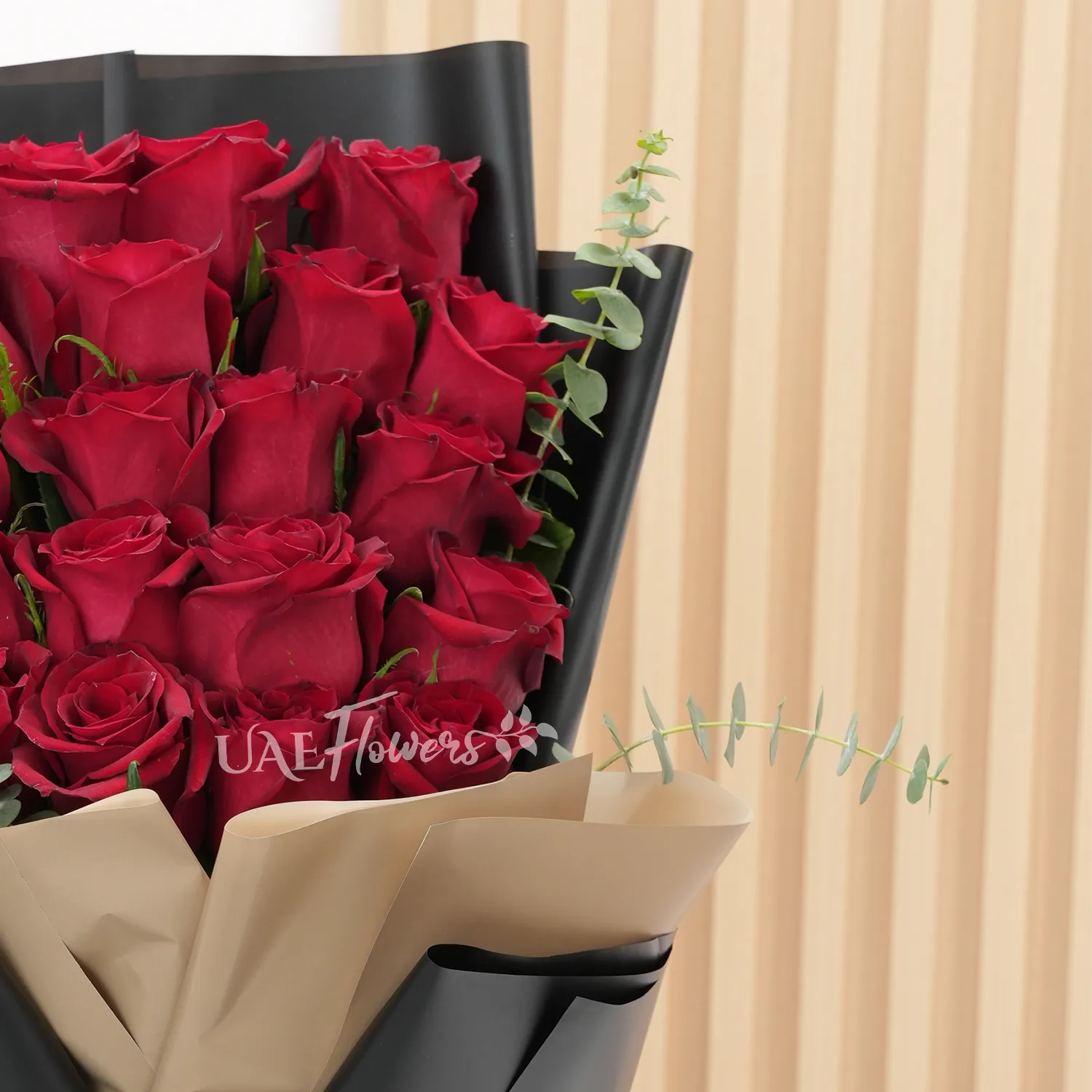 Bouquet of 20 red roses with green fillers in paper packing.
