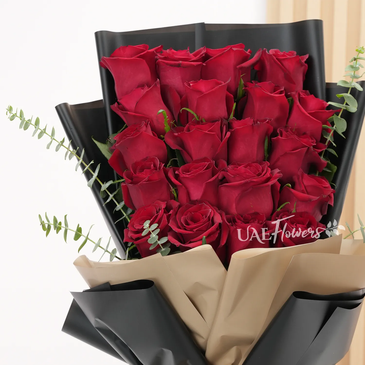 Bouquet of 20 red roses with green fillers in paper packing.