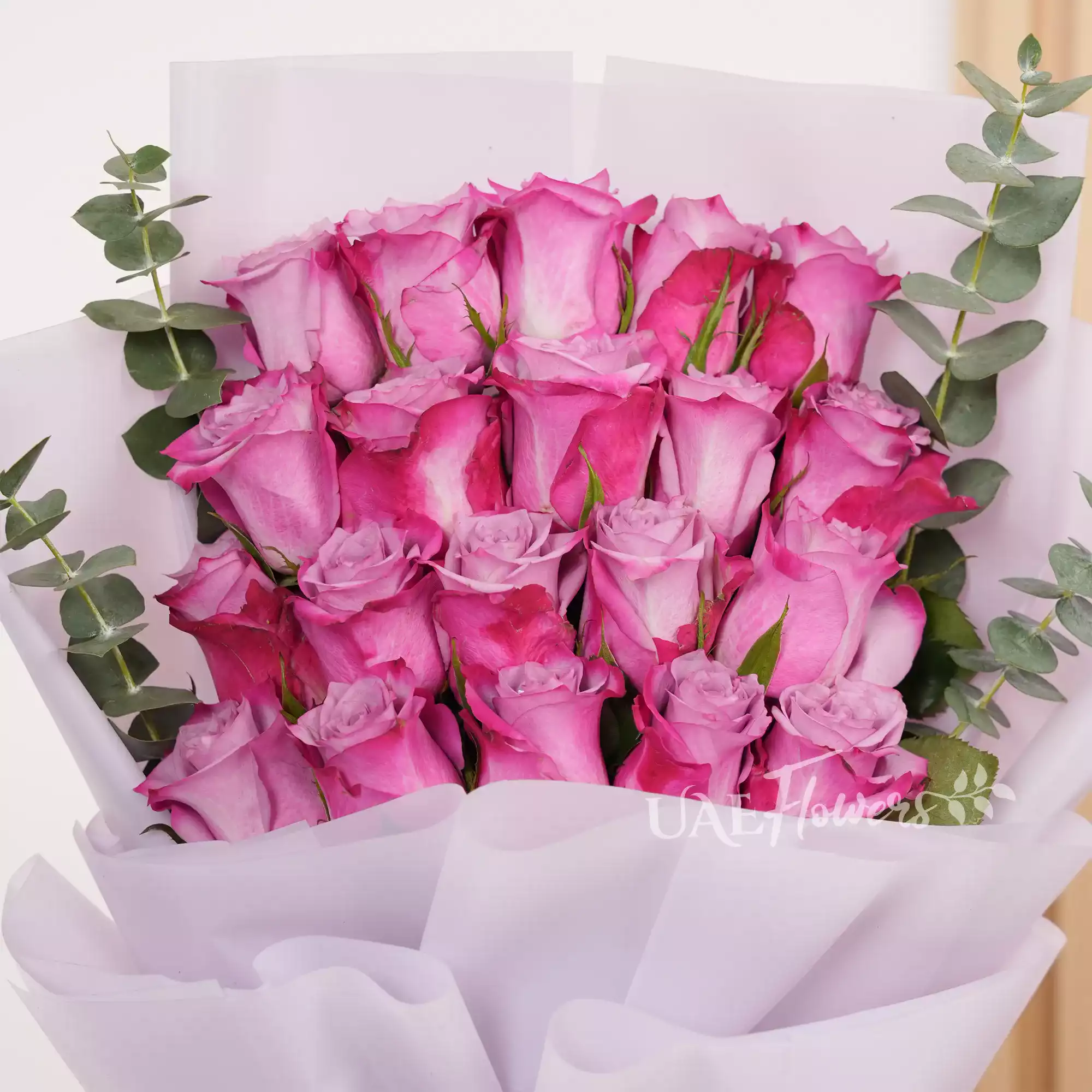 Bouquet of 20 purple roses with eucalyptus leaf in pink paper packing tied with white ribbons.