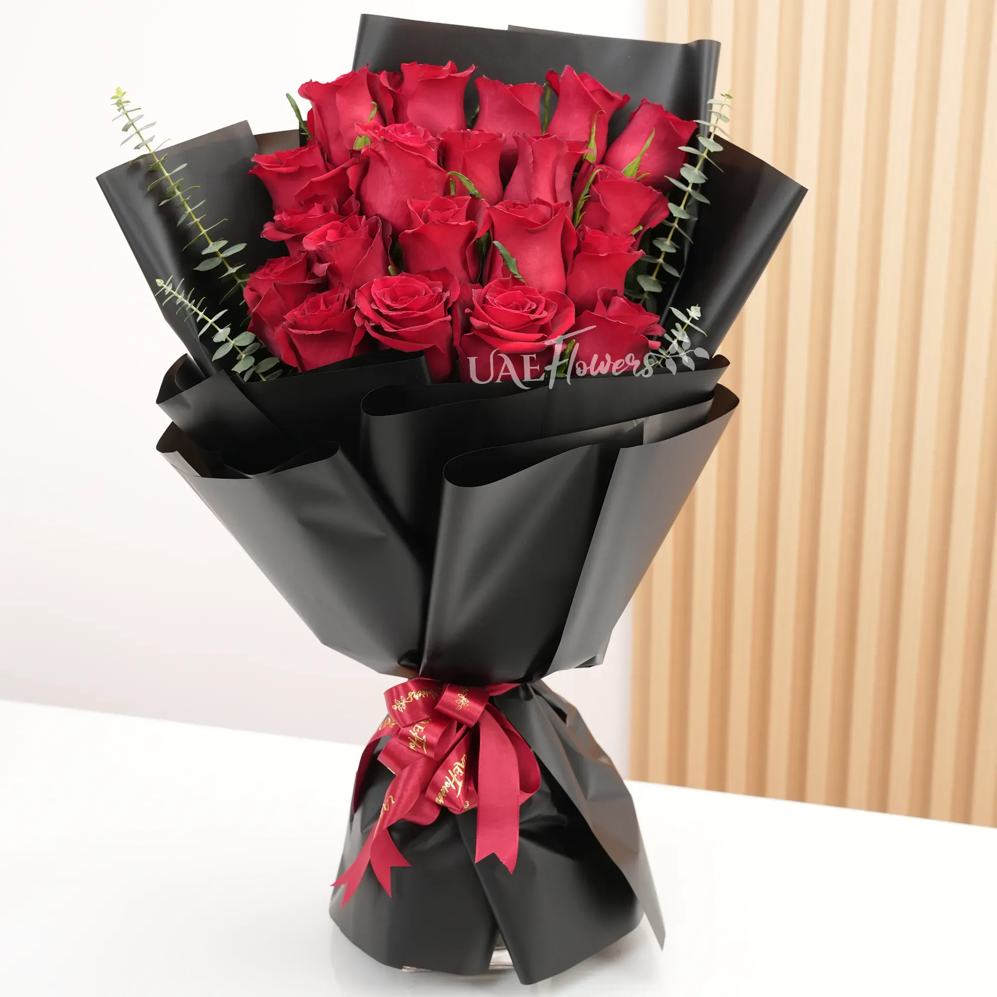 Bouquet of 20 red roses with green and eucalyptus leaf in black paper packing and tied with red ribbons.