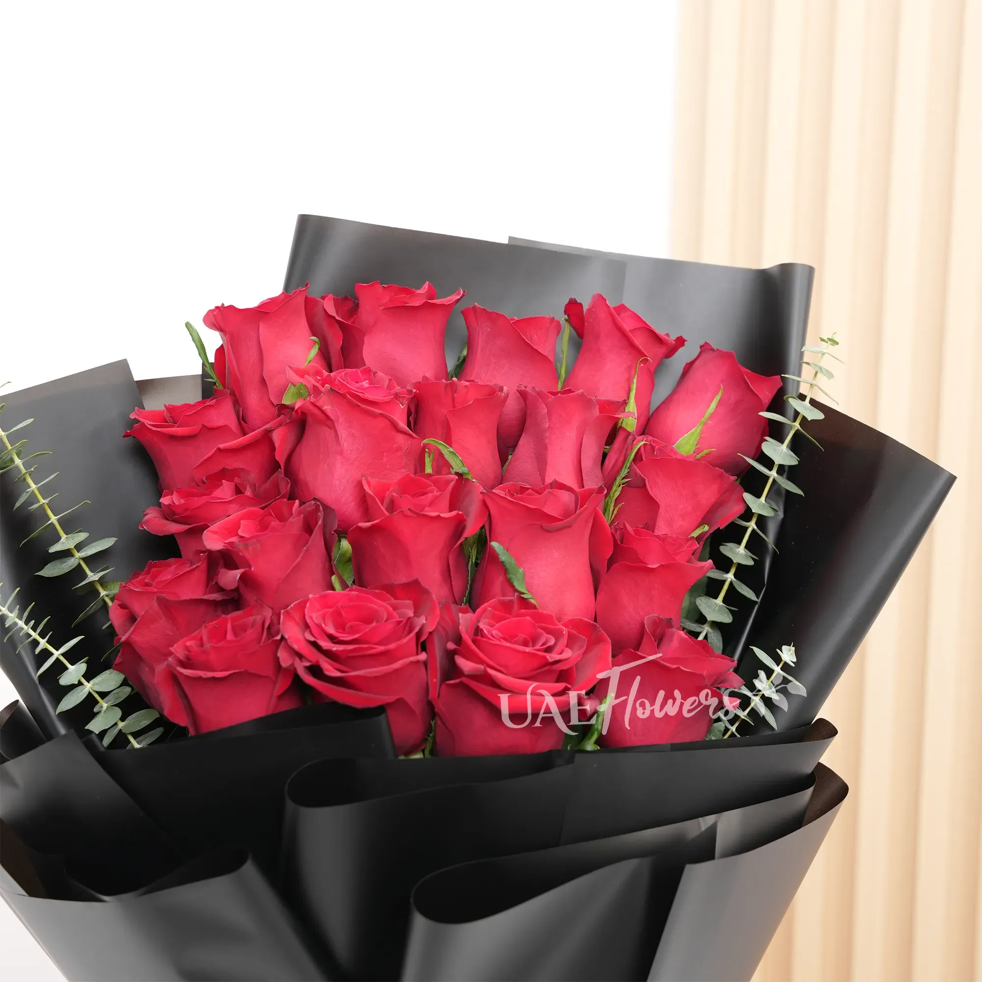Bouquet of 20 red roses with green and eucalyptus leaf in black paper packing and tied with red ribbons.