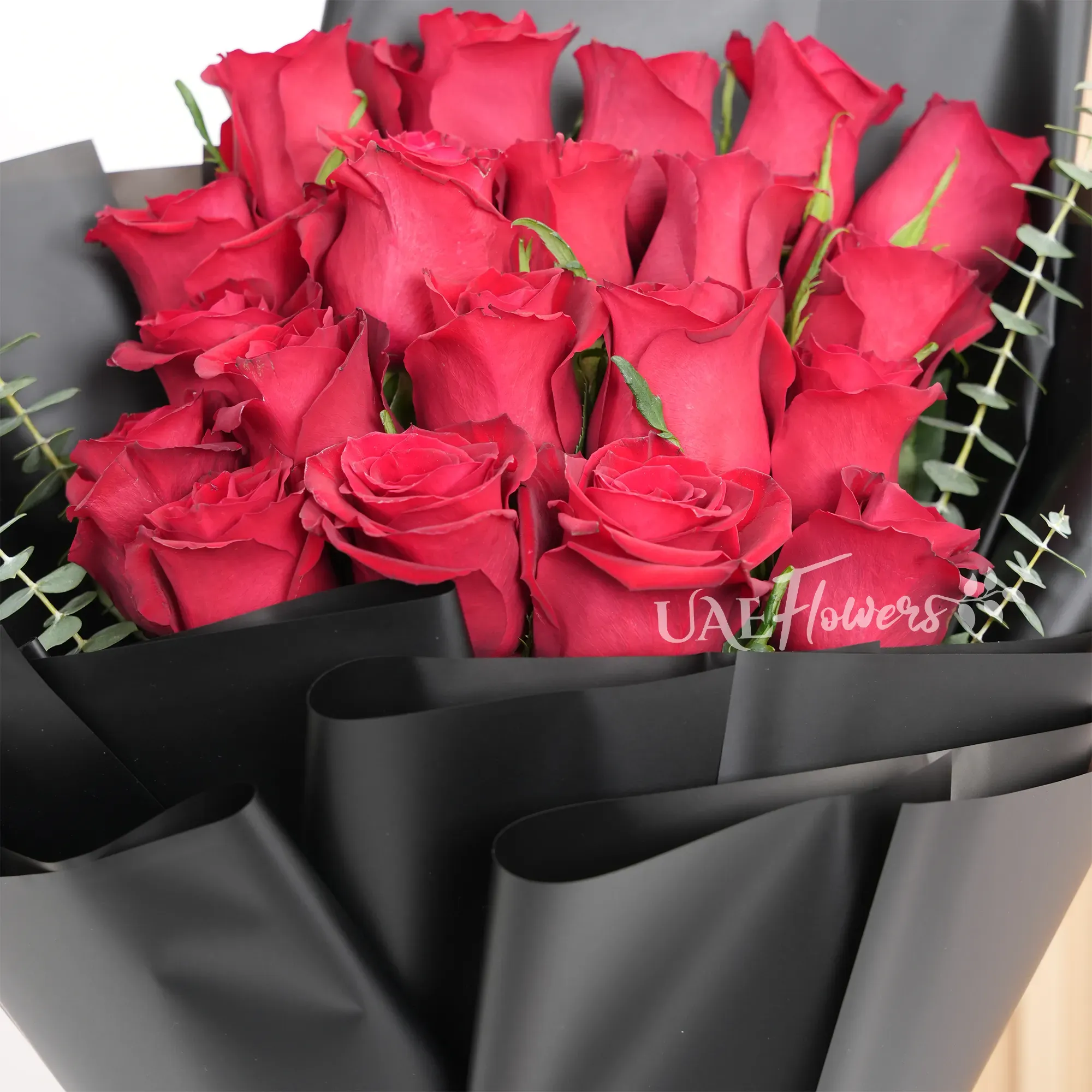 Bouquet of 20 red roses with green and eucalyptus leaf in black paper packing and tied with red ribbons.