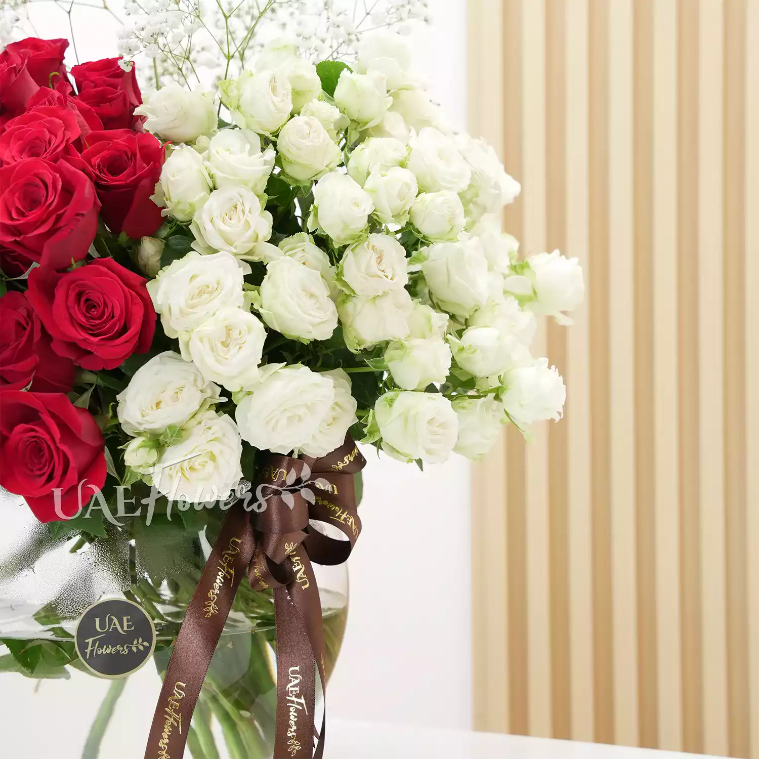 A vase arrangement of 40 red roses and 10 white spray roses with baby's breath and tied with brown ribbons.